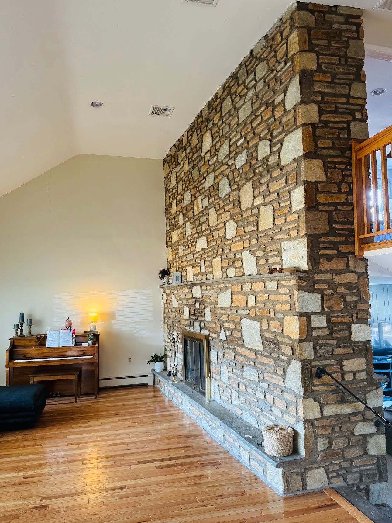 Living room with a tall stone fireplace, hardwood floors, and a small desk lamp against a vaulted ceiling