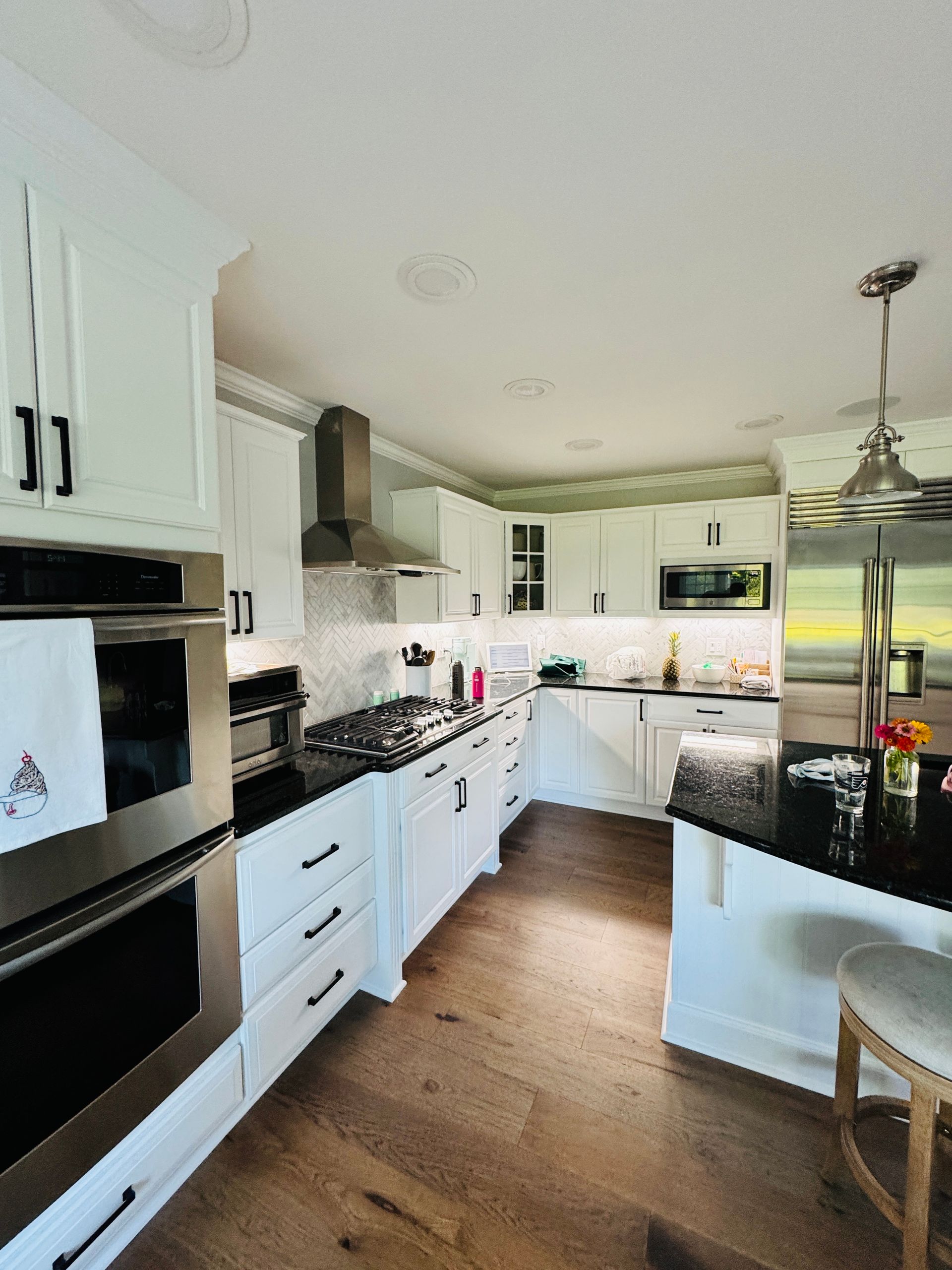 Bright modern white kitchen with black appliances, wood floor, and a stainless steel refrigerator.