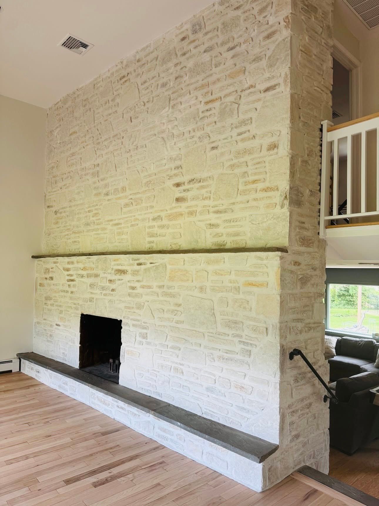 White painted brick fireplace with a long hearth in a bright living room with wood floors and staircase railing.