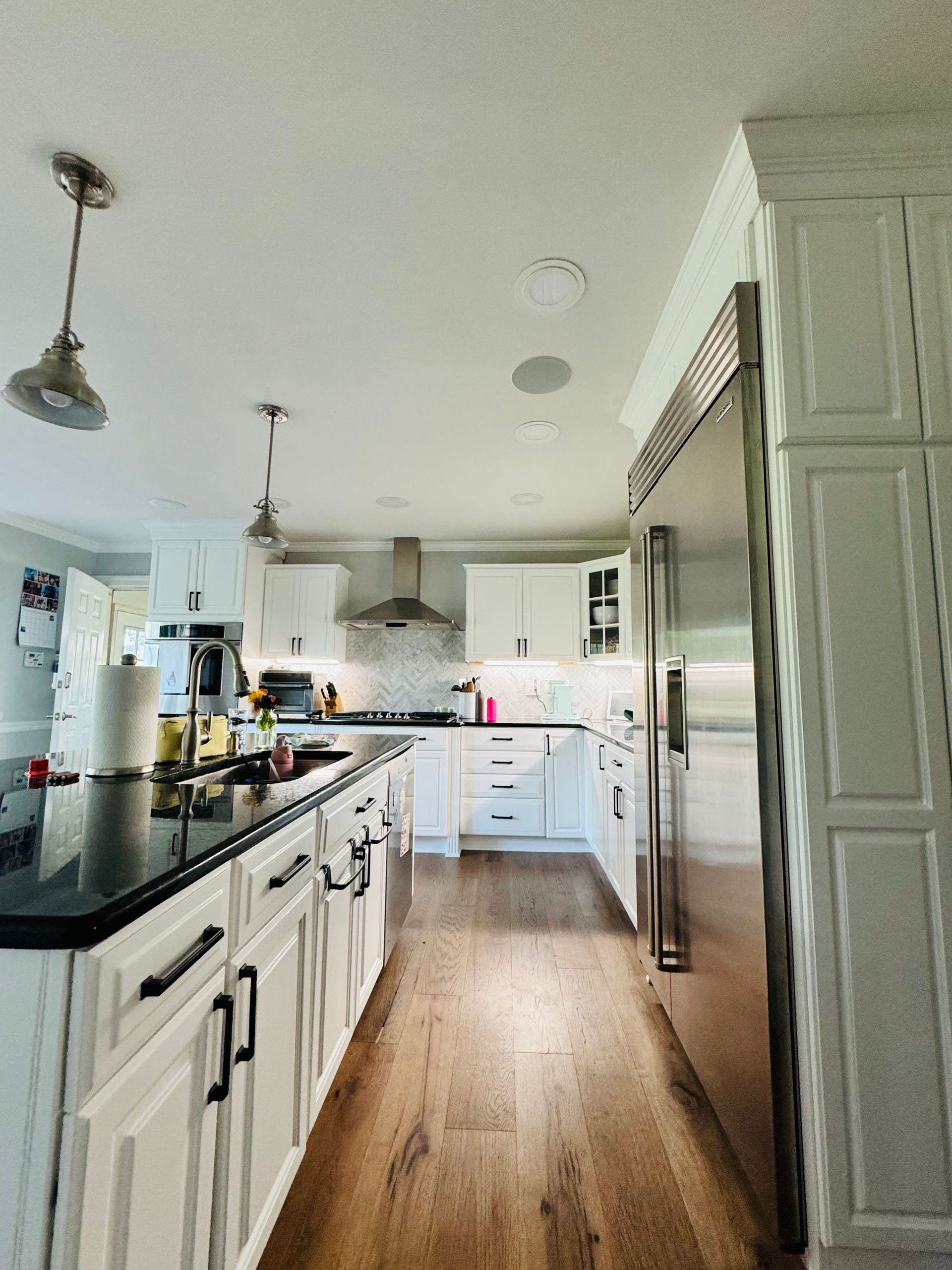 Bright kitchen with white cabinets, stainless appliances, wood floor, and long island under pendant lights