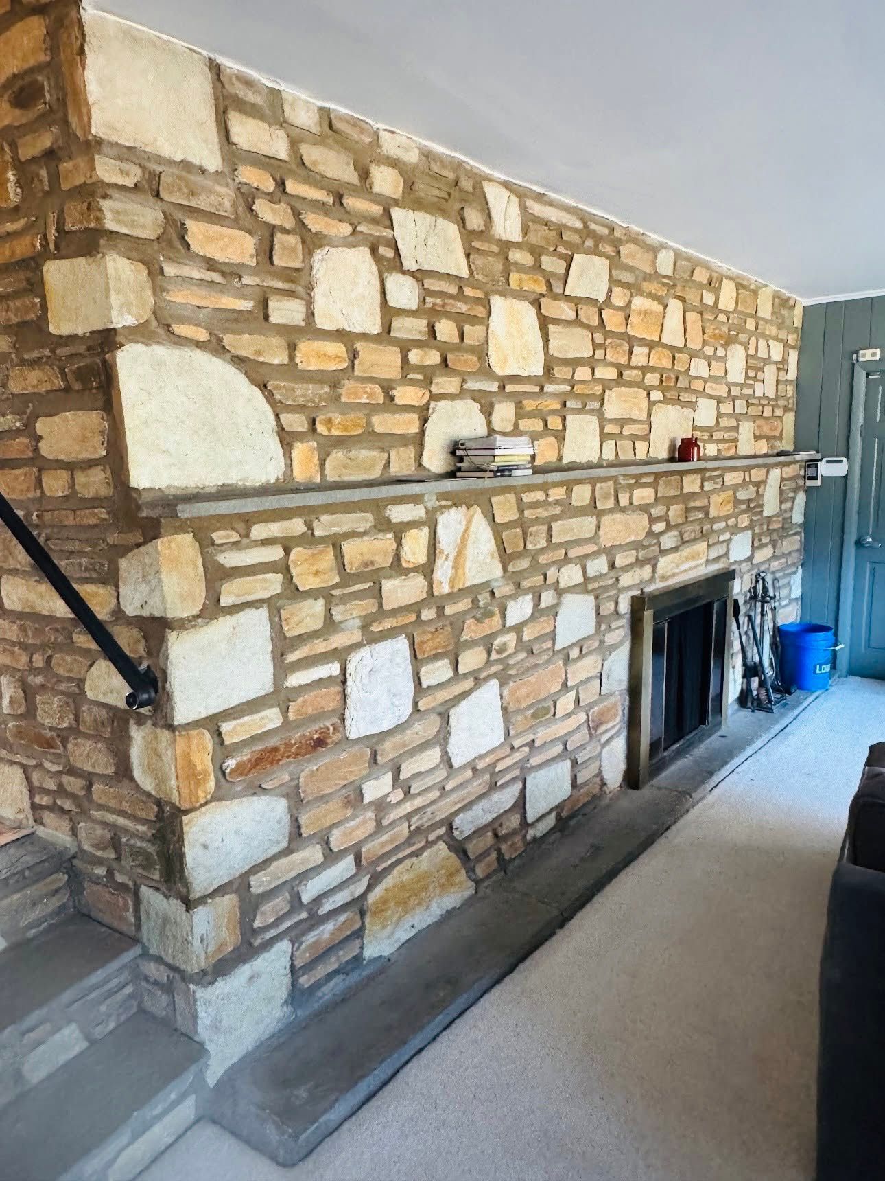 Stone fireplace wall in a living room, with a dark firebox and a staircase railing on the left.