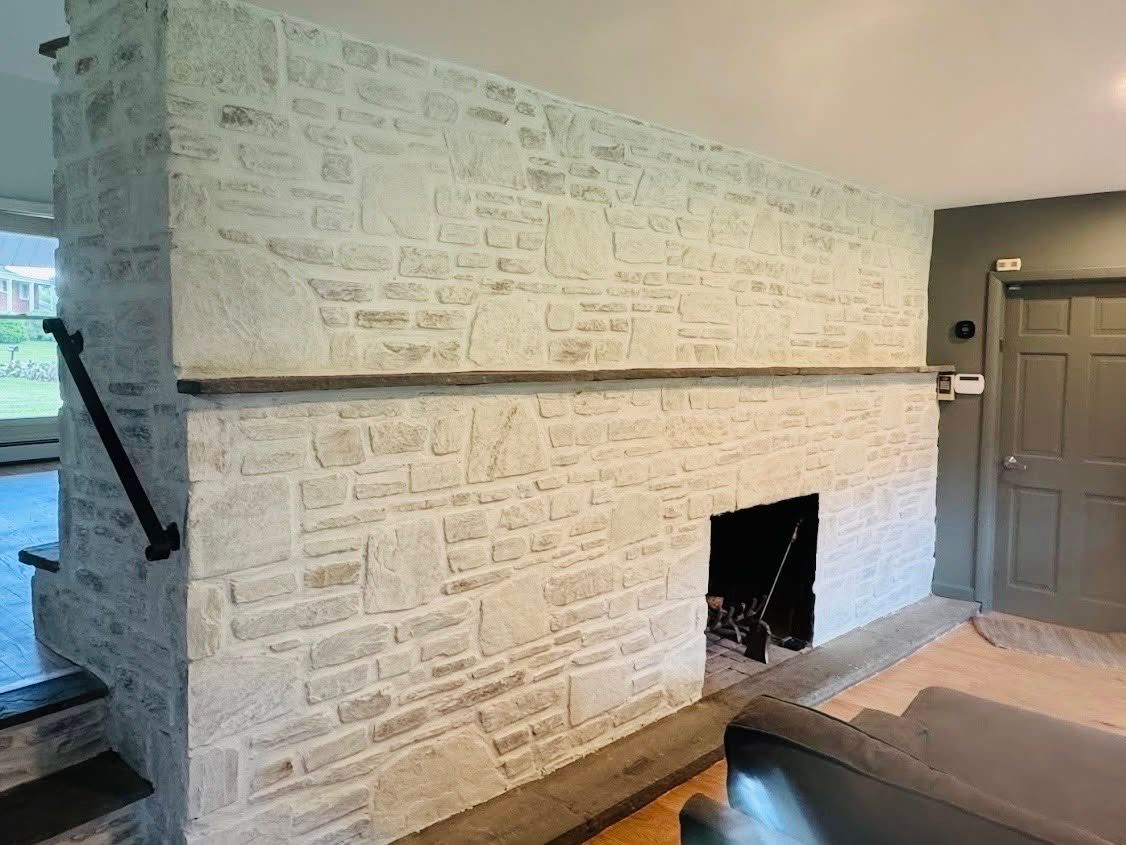Bright stone fireplace with dark wood mantel in a living room beside a gray door and stairs