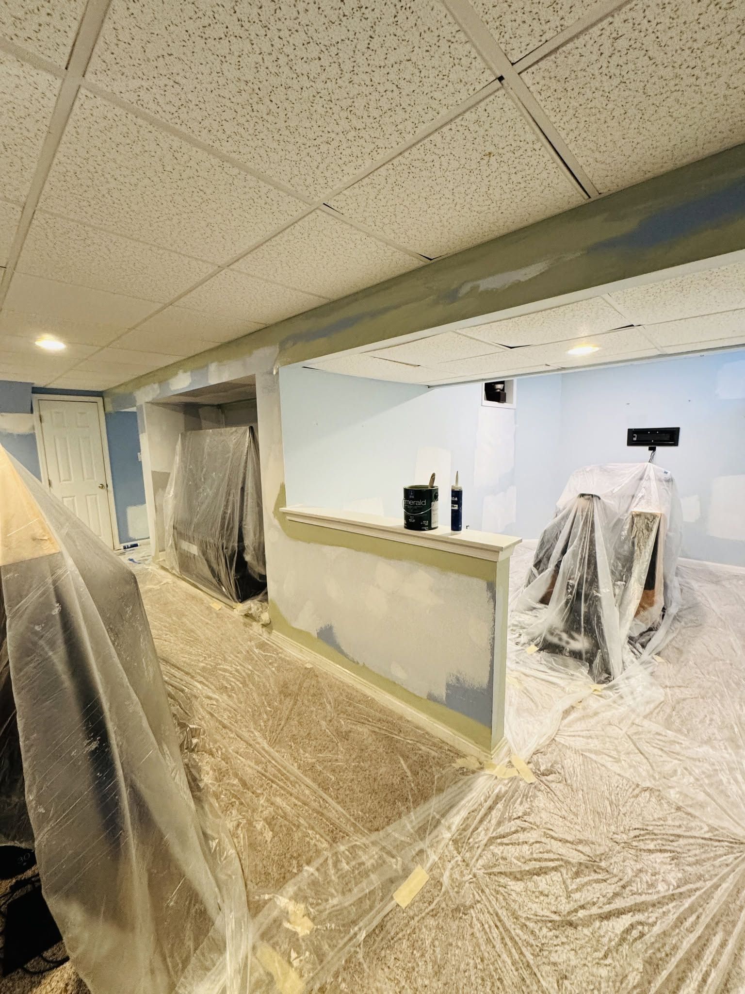 Renovation area with plastic-covered walls, drop ceiling, and dust-covered floor in an unfinished room