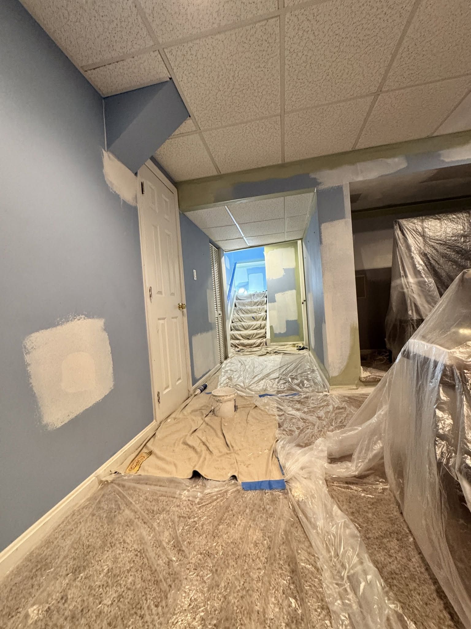 Construction area with blue walls, plastic sheeting, and unfinished flooring in a hallway