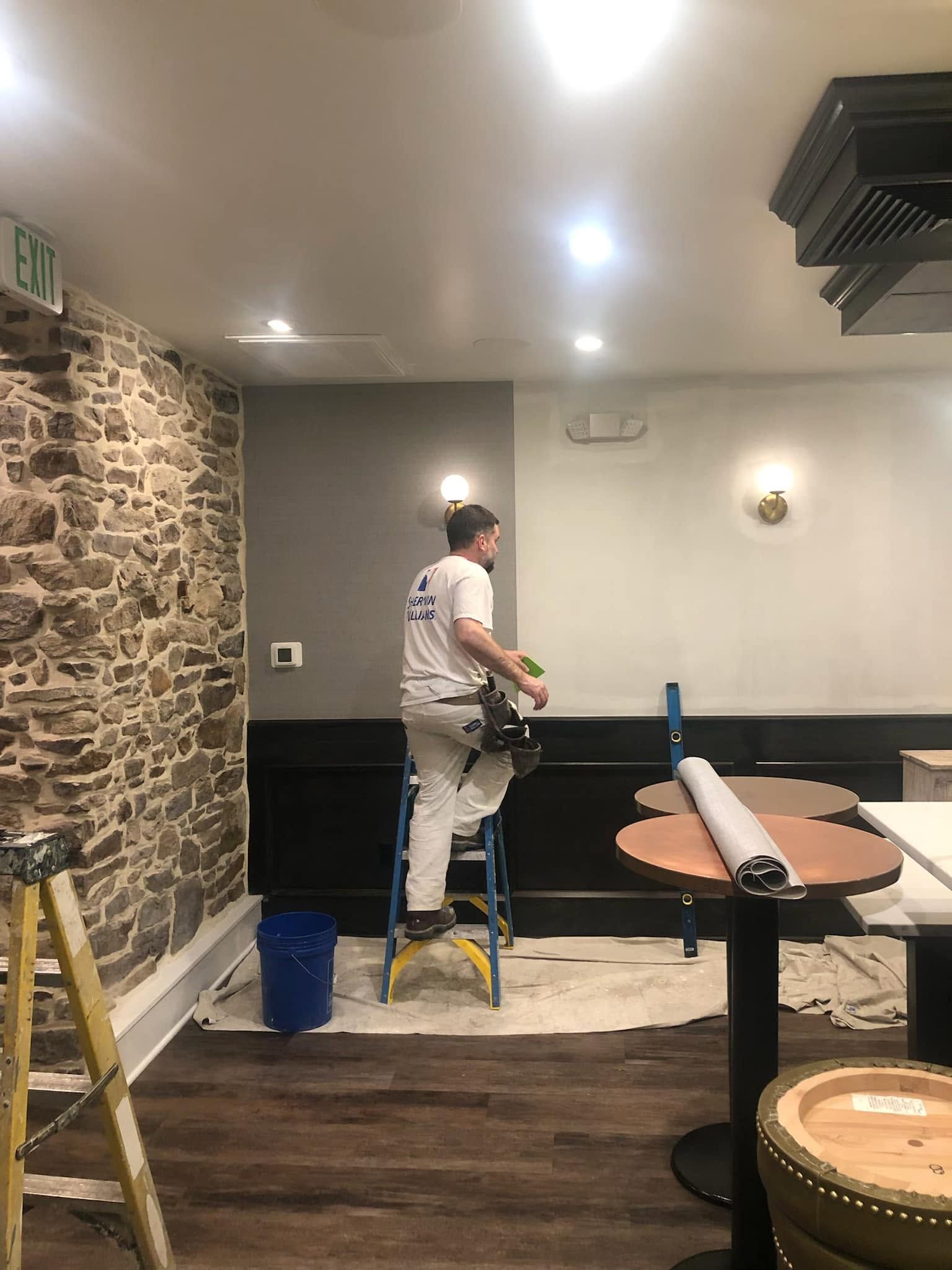 Worker painting a wall in a restaurant interior with stone accent wall and ceiling lights