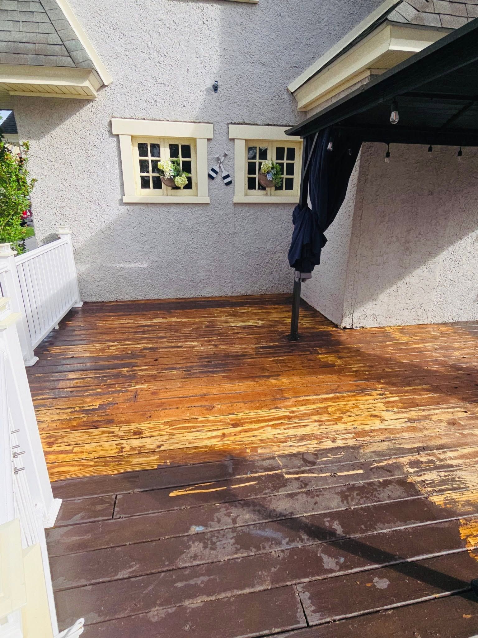 Weathered wooden patio/deck with two windows, white fence, and a covered area on the right