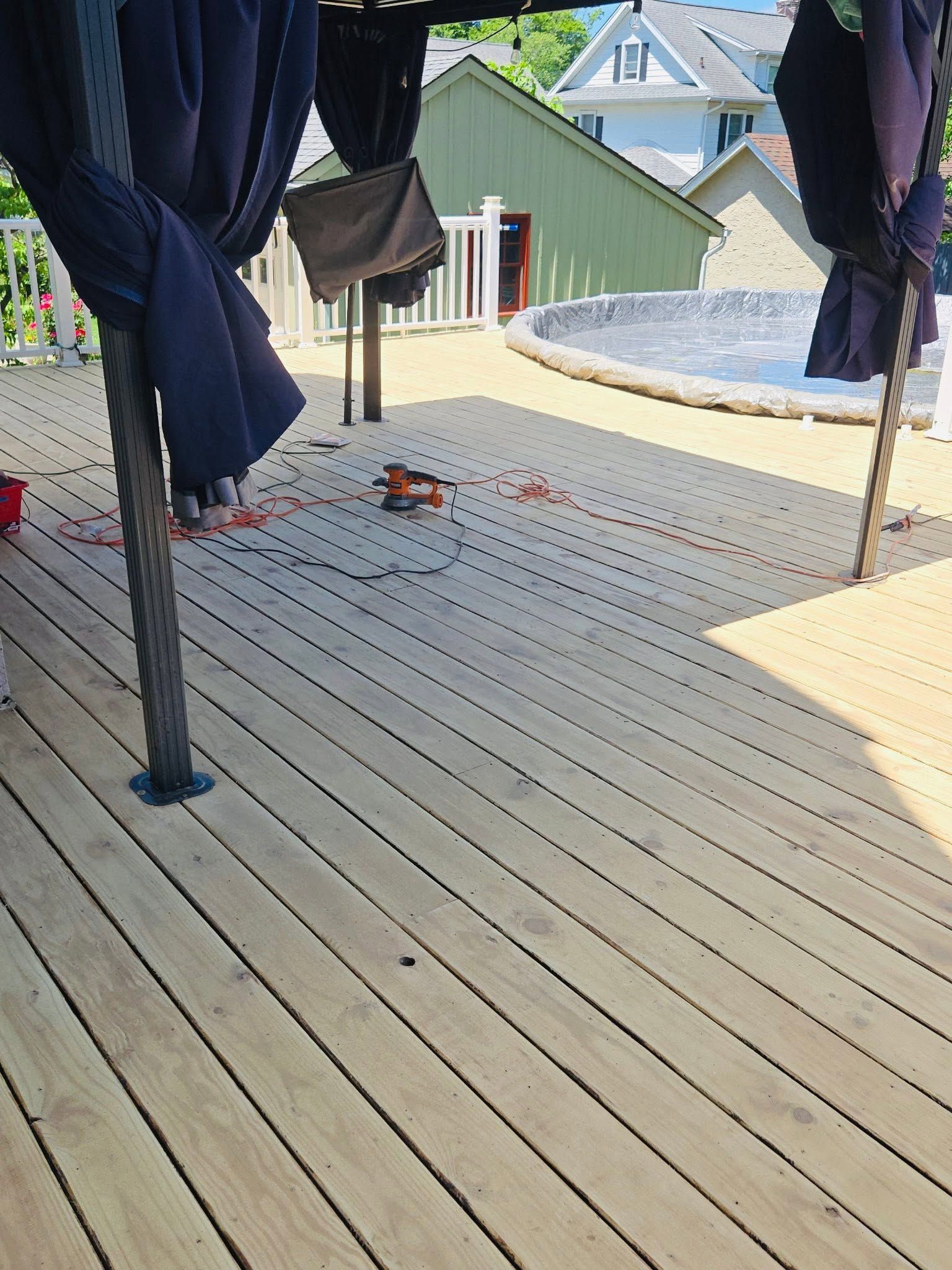 Wooden deck with black posts and draped fabric, overlooking neighboring houses and a gravel yard.