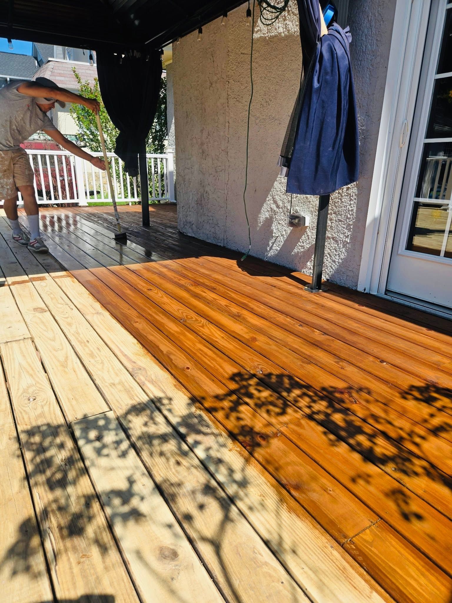 Sunny wooden porch with a person standing at the left edge and a blue jacket hanging on the wall