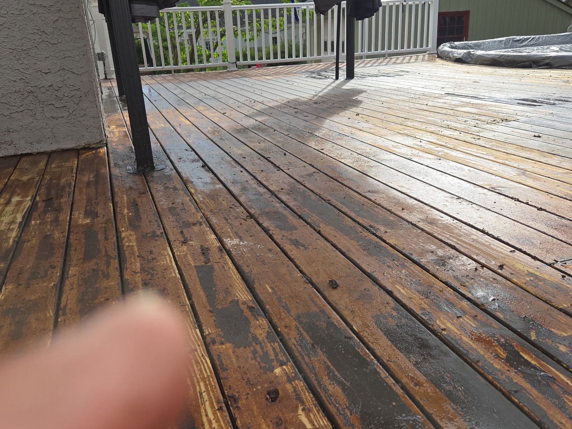 Wet wooden deck with railing and a blurred finger in the foreground