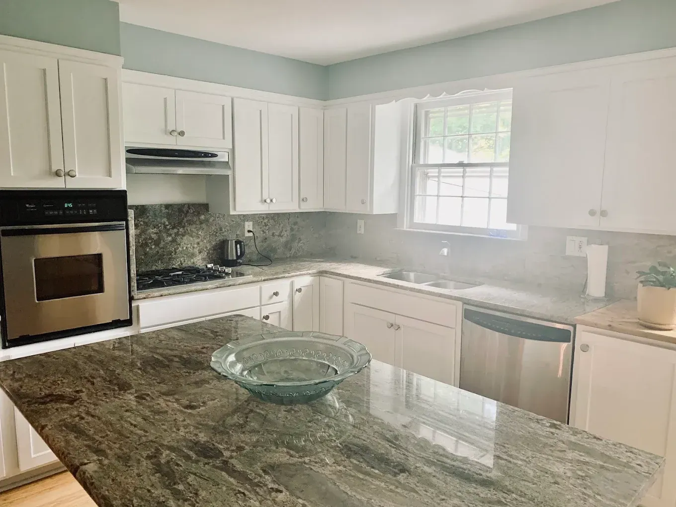 Bright kitchen with white cabinets, granite island, and sunlight through a window.