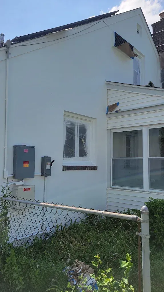 White house exterior with small porch, window, utility boxes, and chain-link fence in front