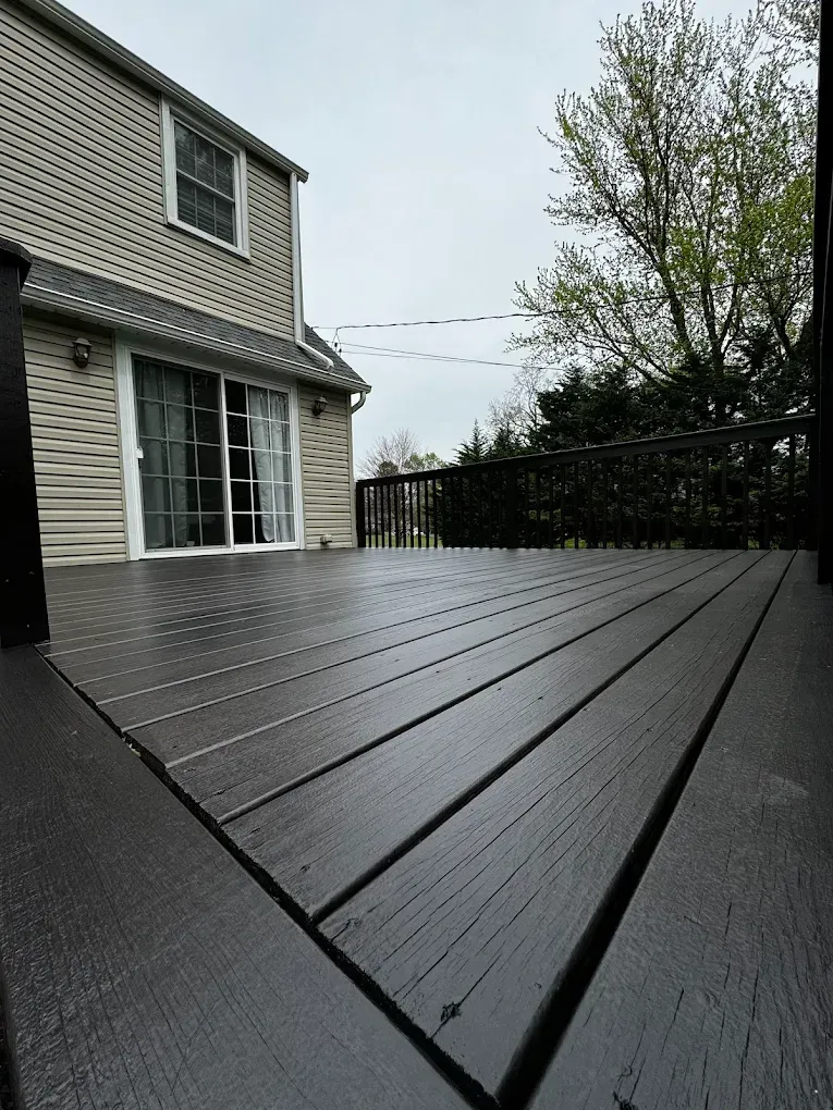 Dark wood deck beside a gray house, viewed from a low angle on an overcast day