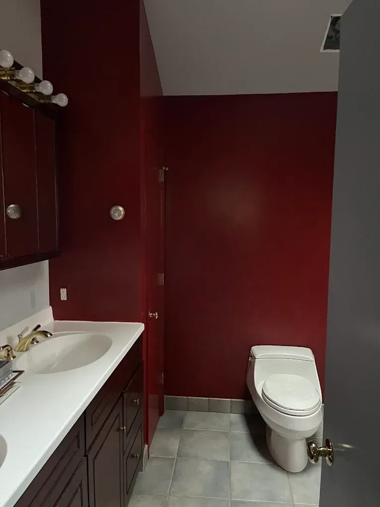 Small bathroom with burgundy walls, gray tile floor, white sink vanity, and toilet.