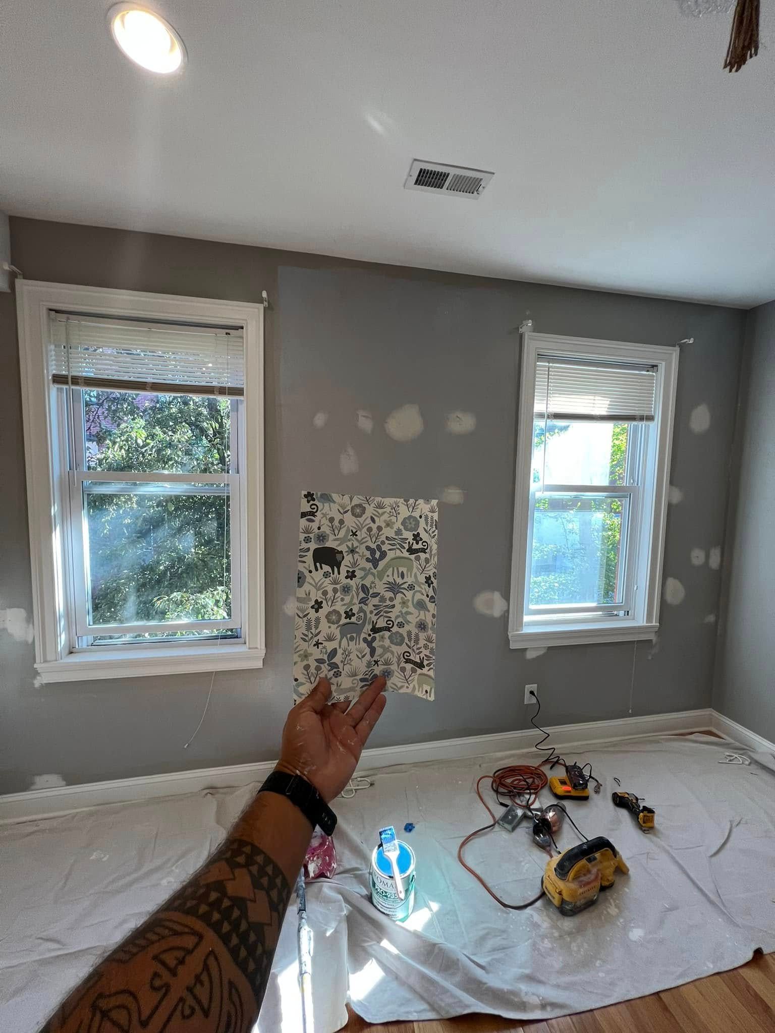 Paint swatches on a gray wall between two windows, with a hand pointing in a room under renovation.