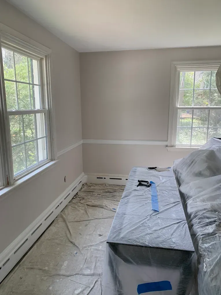 Empty room with windows, plastic-covered furniture, and floor protection during painting or renovation