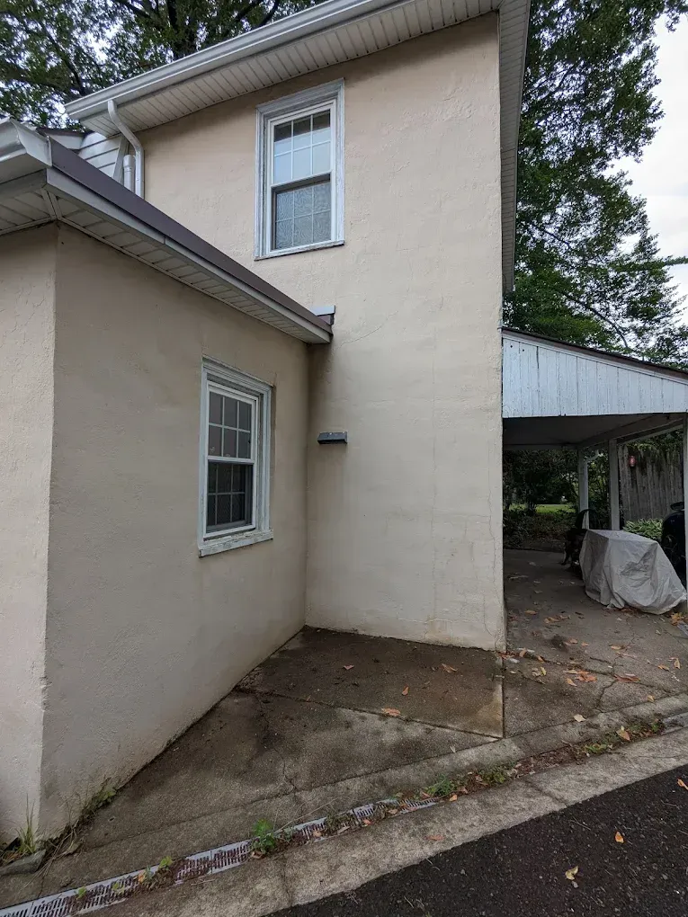 Beige house exterior with a window, narrow side yard, and a carport-like covered area.