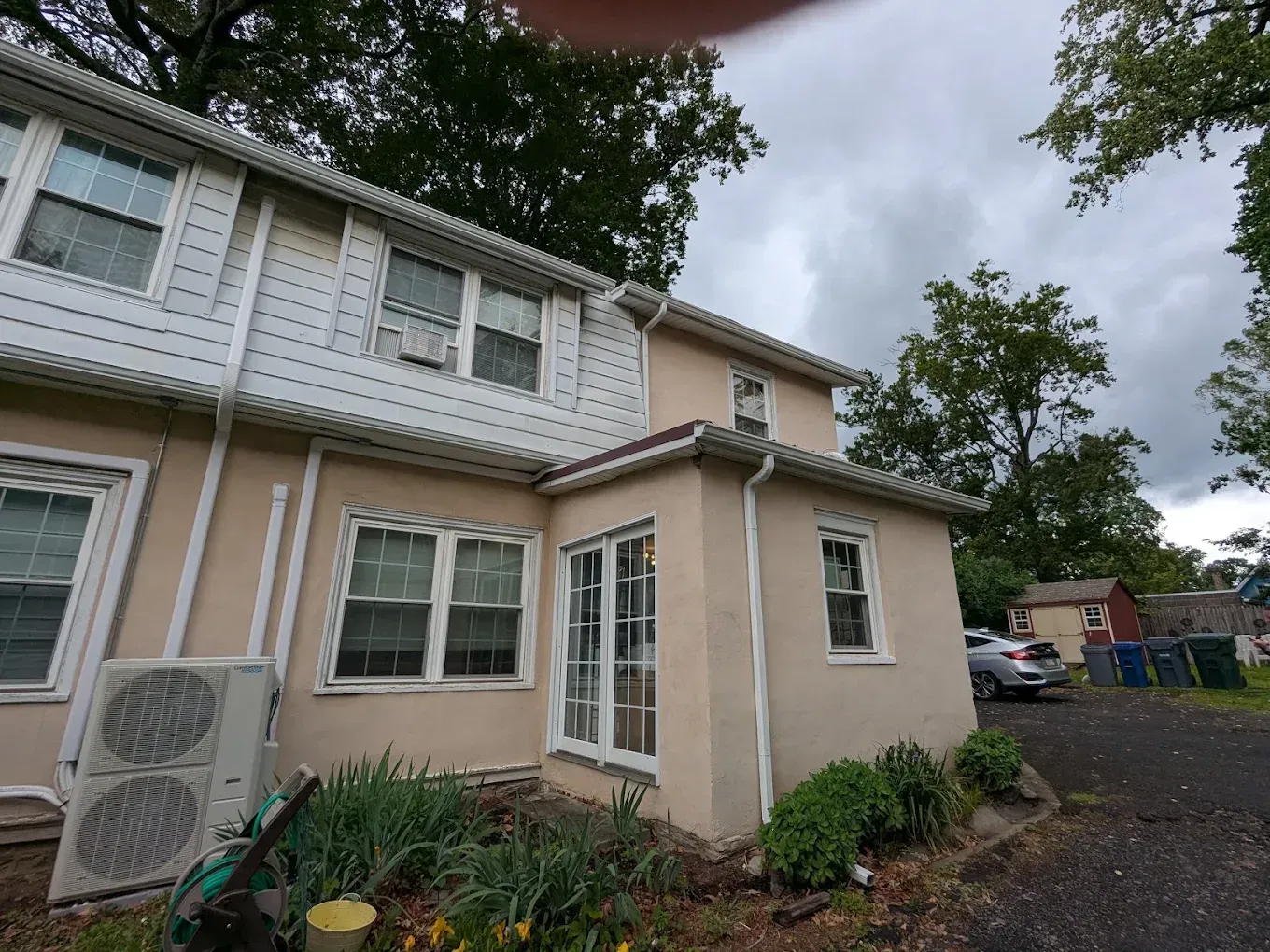 Beige two-story house with white trim, front garden, and cloudy sky overhead