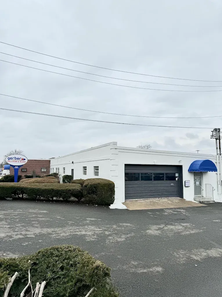 White commercial building with a blue awning, black garage door, and parking lot under overcast skies