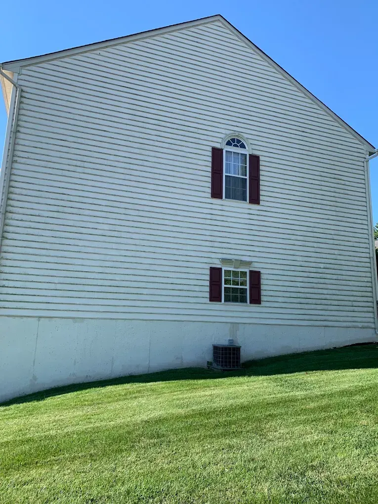 Side view of a beige house with maroon shutters and a grassy lawn under a blue sky
