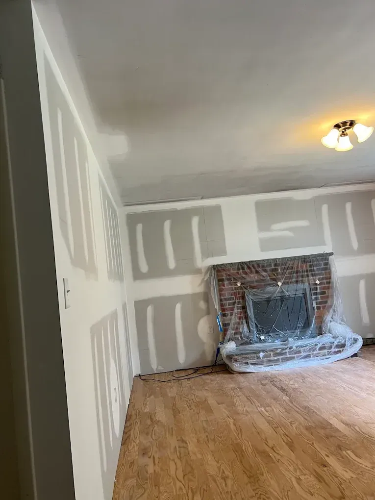 Renovated room with drywall patches, hardwood floor, and a fireplace under plastic sheeting