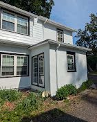 White two-story house exterior with blue trim, porch, and garden beds along a gravel driveway