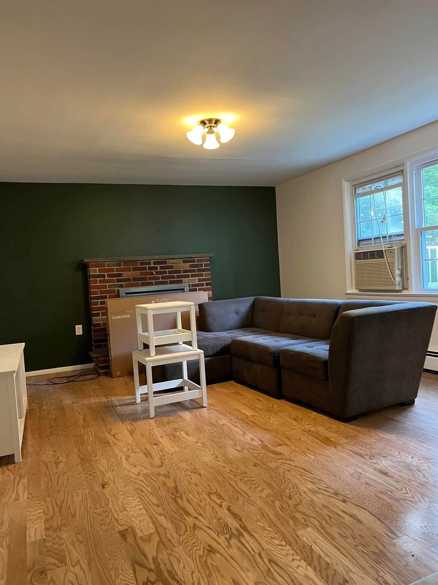 Living room with gray sectional, green accent wall, fireplace, and hardwood floors