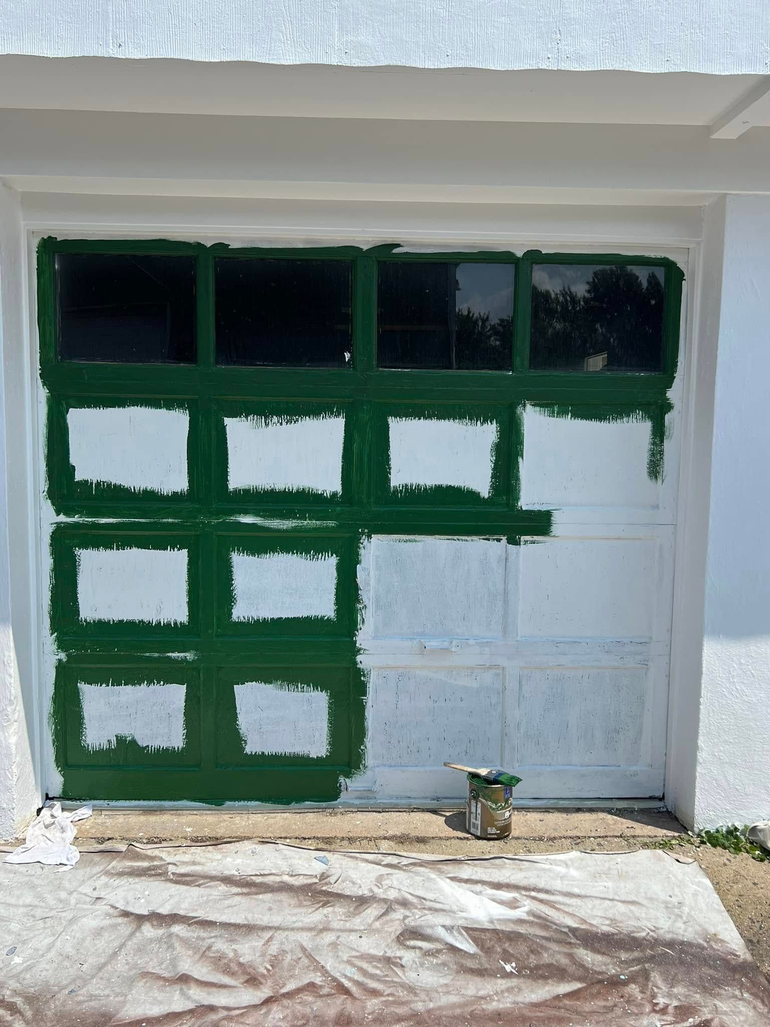Garage door with green and white painted test squares and a paint can on the ground.