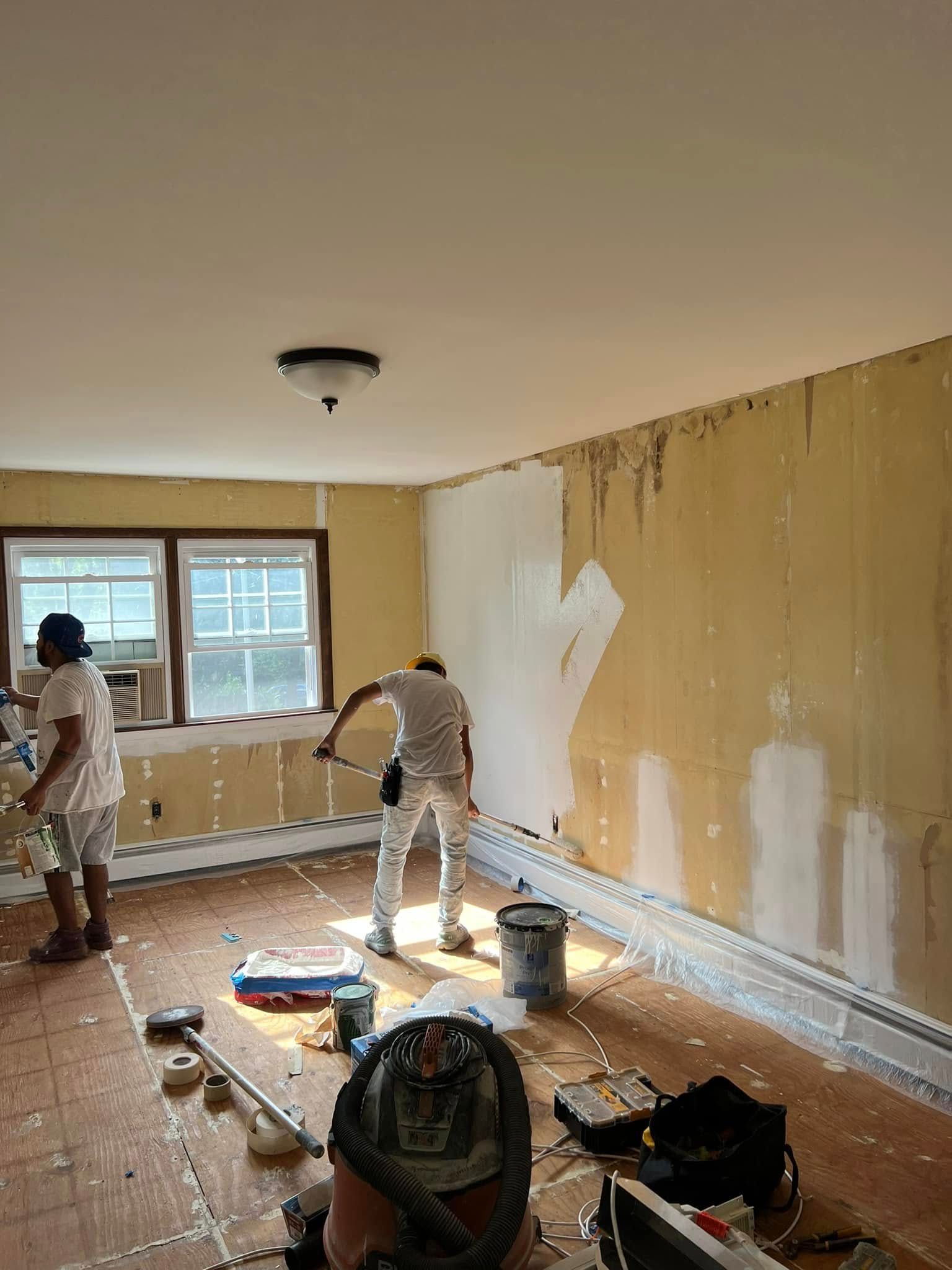 Workers painting and patching walls in a room with tiled floor and large window