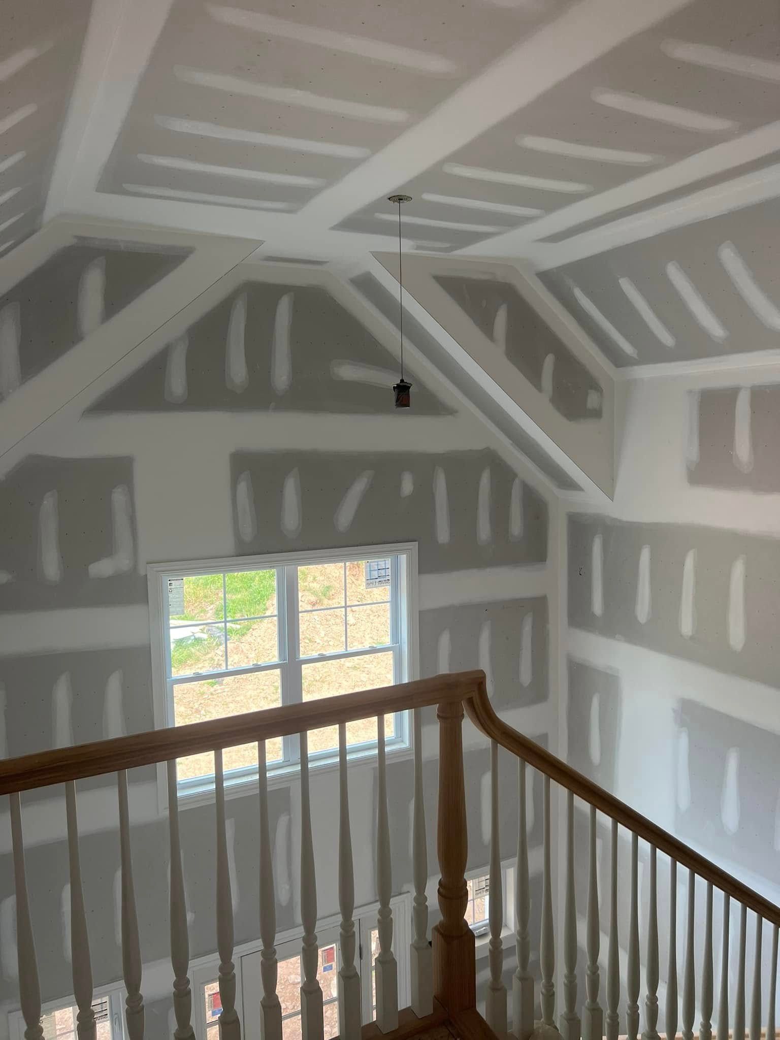 Unfinished attic with gray drywall, exposed beams, and a wooden railing overlooking the space