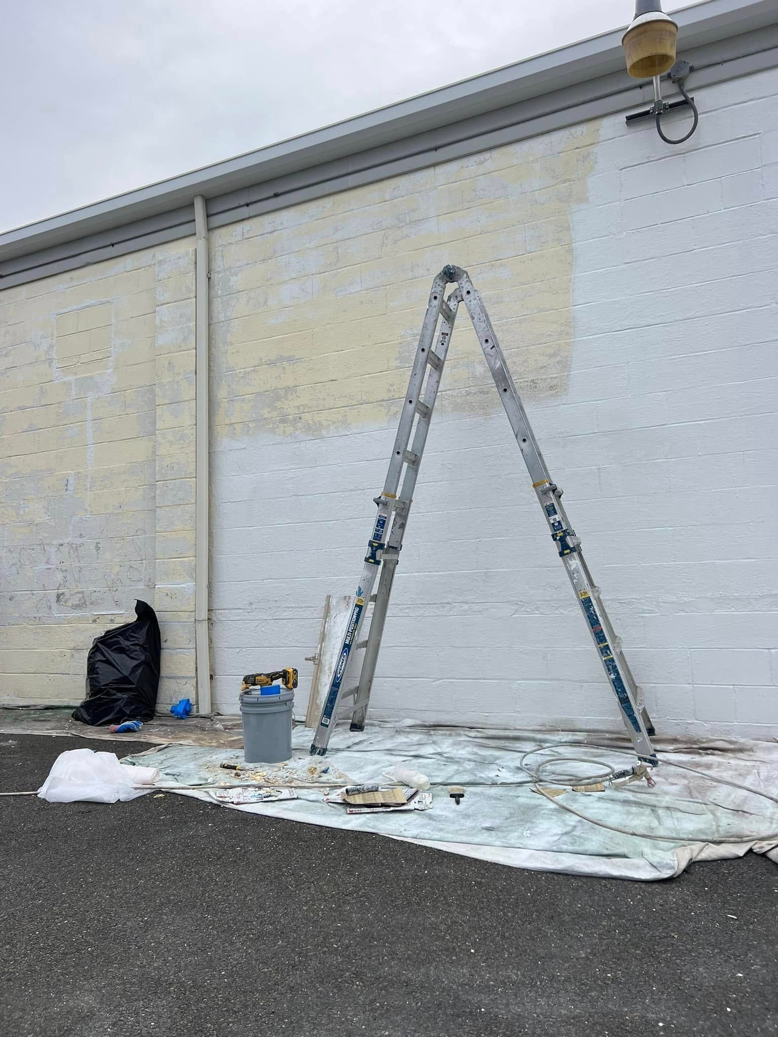 Ladder and paint supplies against a white wall, with drop cloths spread on the ground.