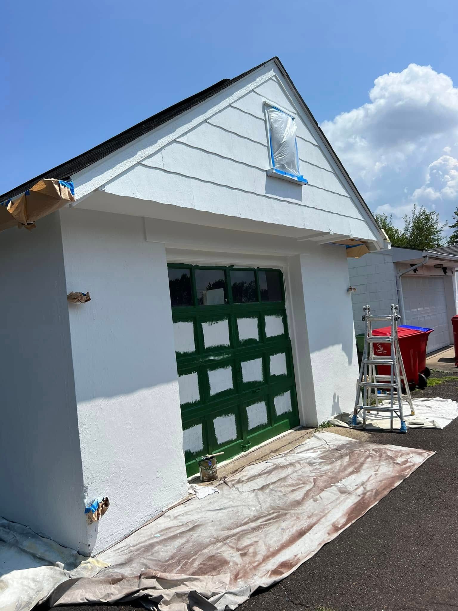 White garage with green door and ladder, under construction on a sunny day