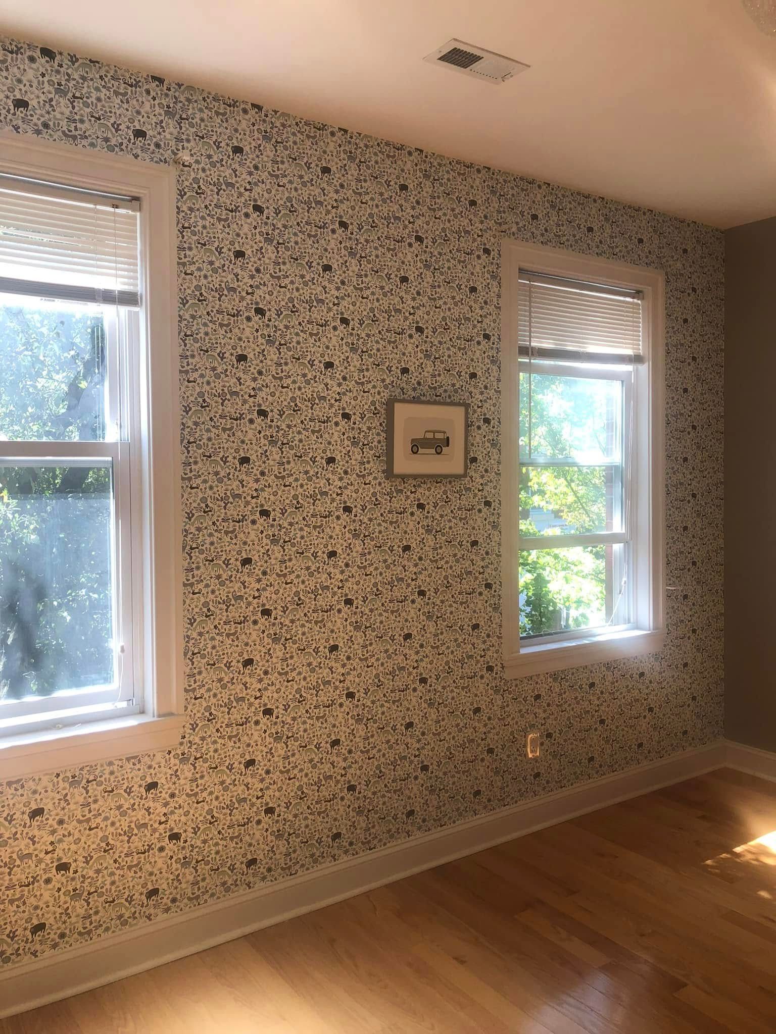 Empty room with patterned wallpaper, two windows, wood floor, and a small framed picture on the wall