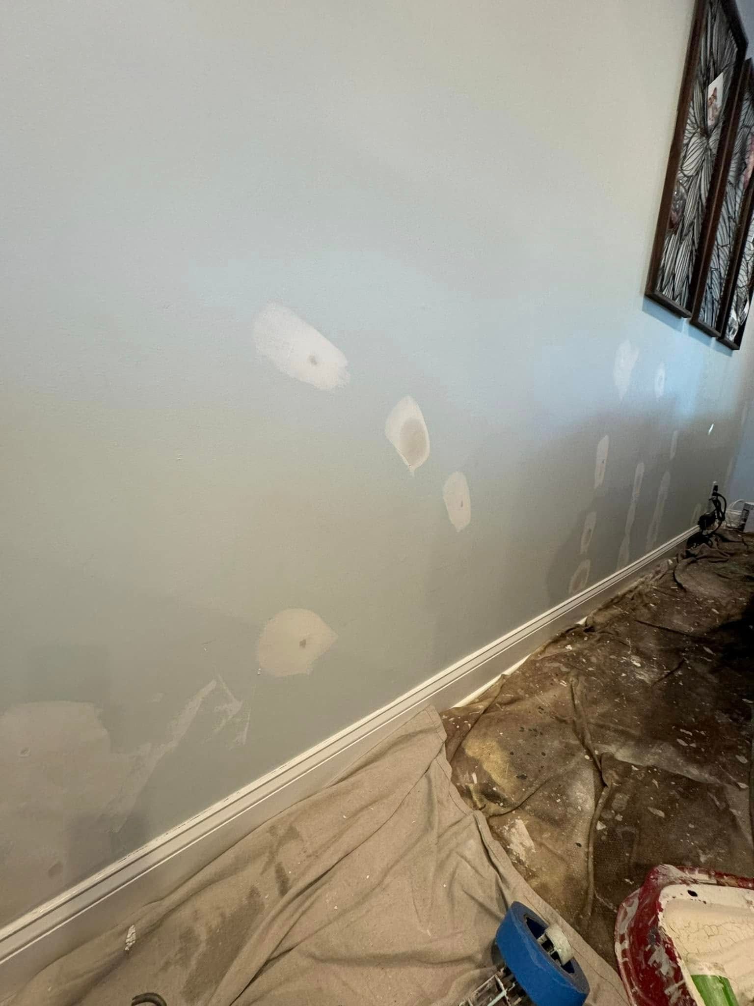Interior wall with several white patch repairs above a baseboard in a room under renovation.