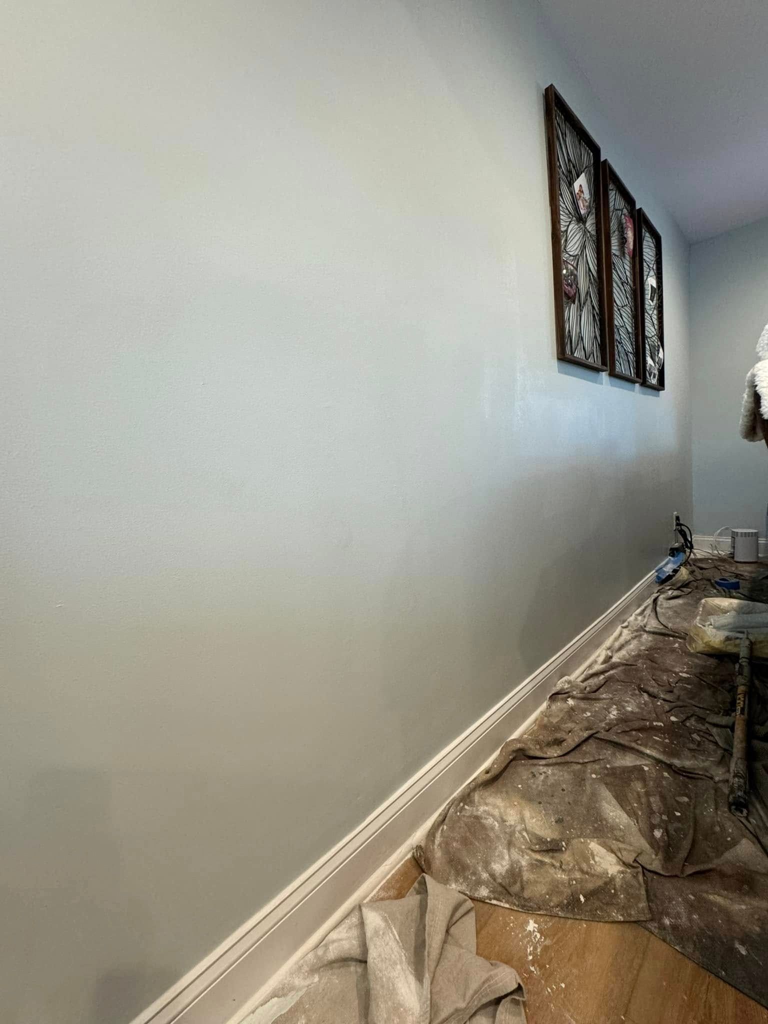 Empty hallway with white walls, framed art, and a floor covered in protective plastic during painting.