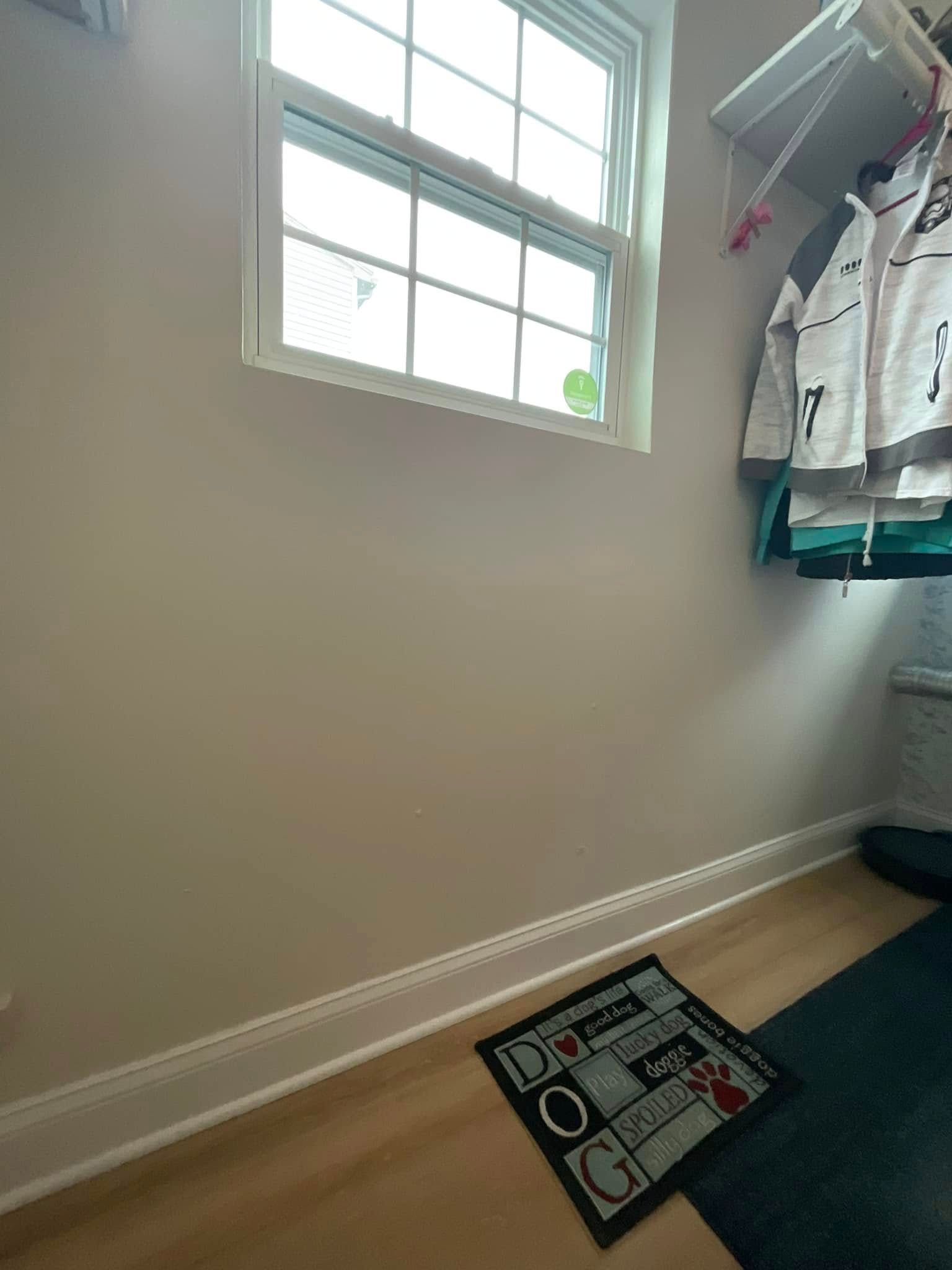 Small empty room with a window, beige walls, hanging clothes, and a sign on the floor