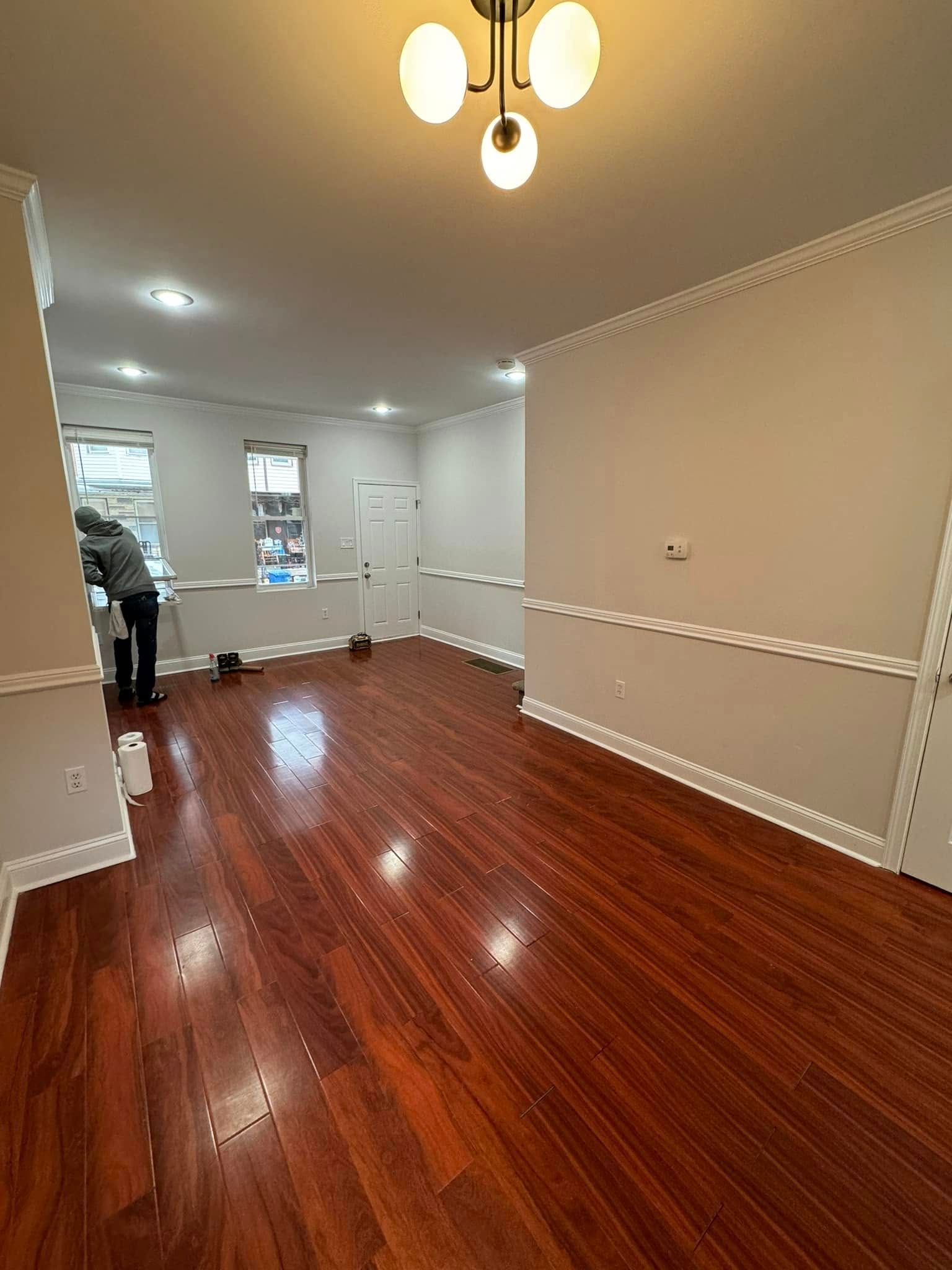Empty room with glossy red hardwood floors, beige walls, and ceiling lights; person stands near the back left.