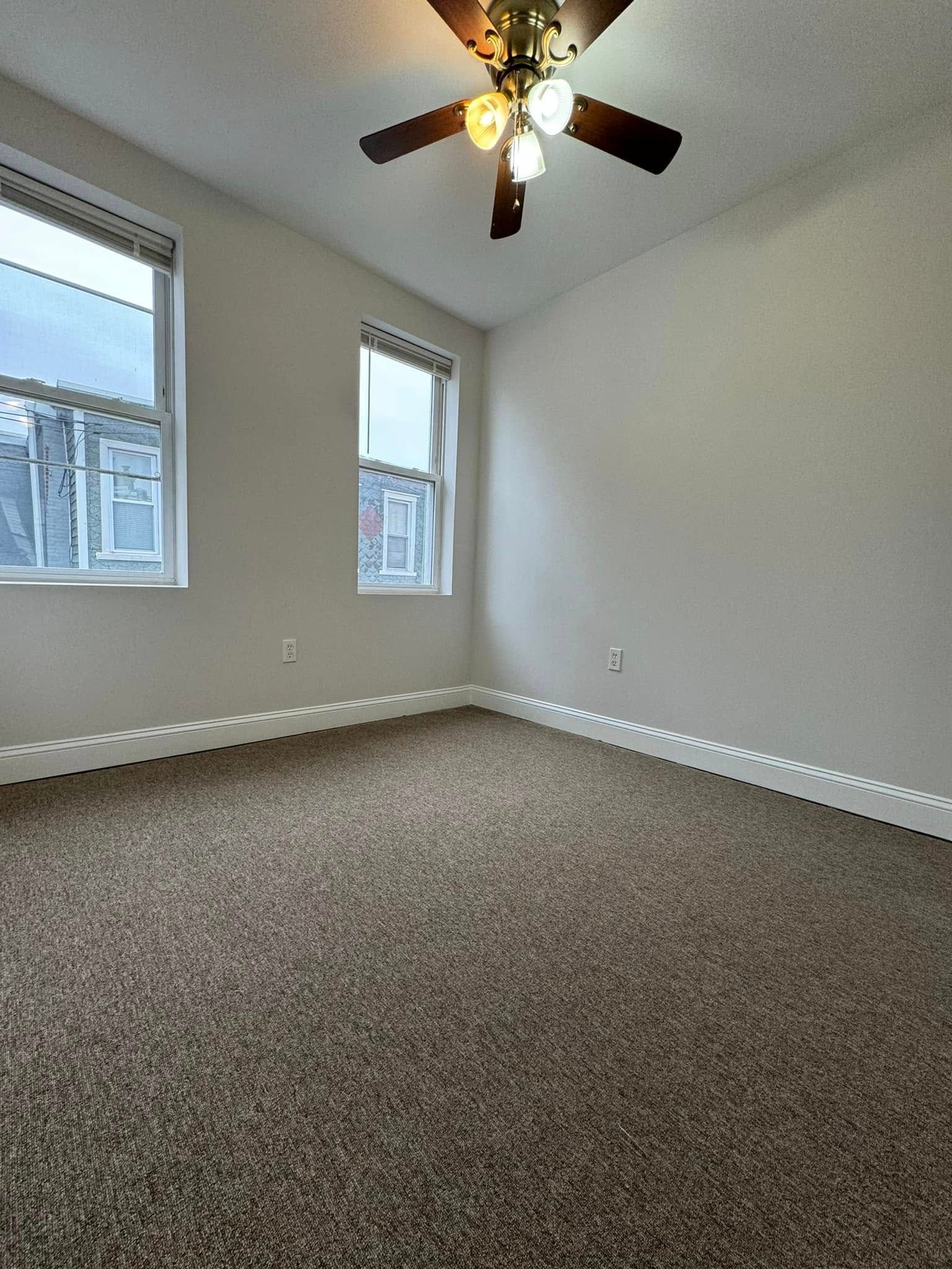 Empty carpeted bedroom with two windows and a ceiling fan light visible.