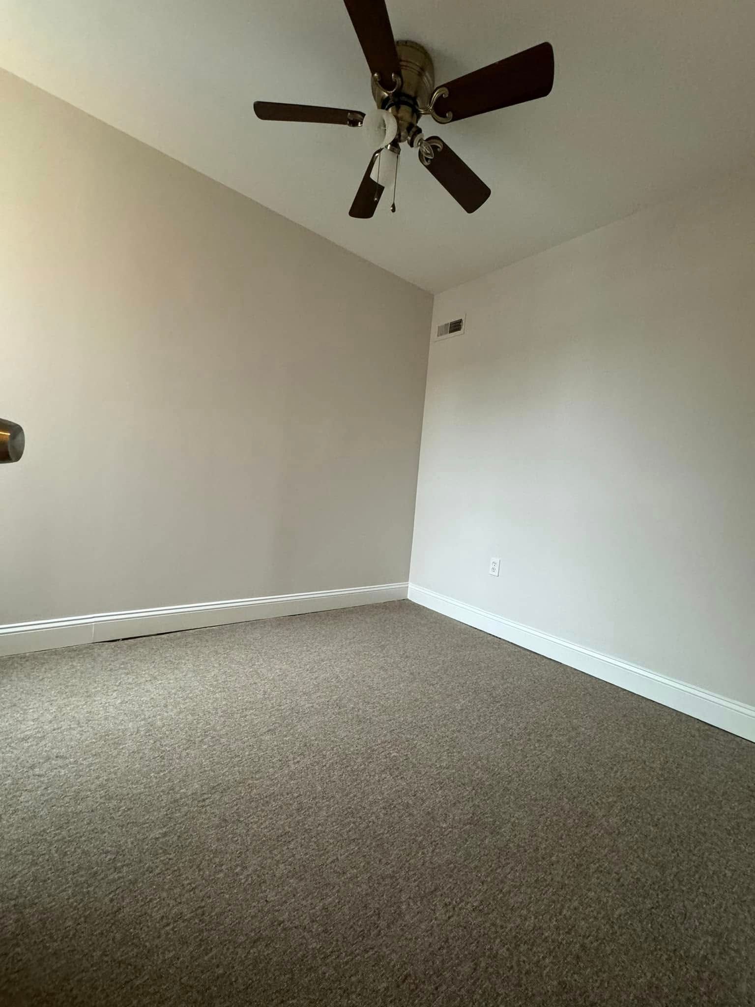 Empty carpeted room with white walls and a ceiling fan.