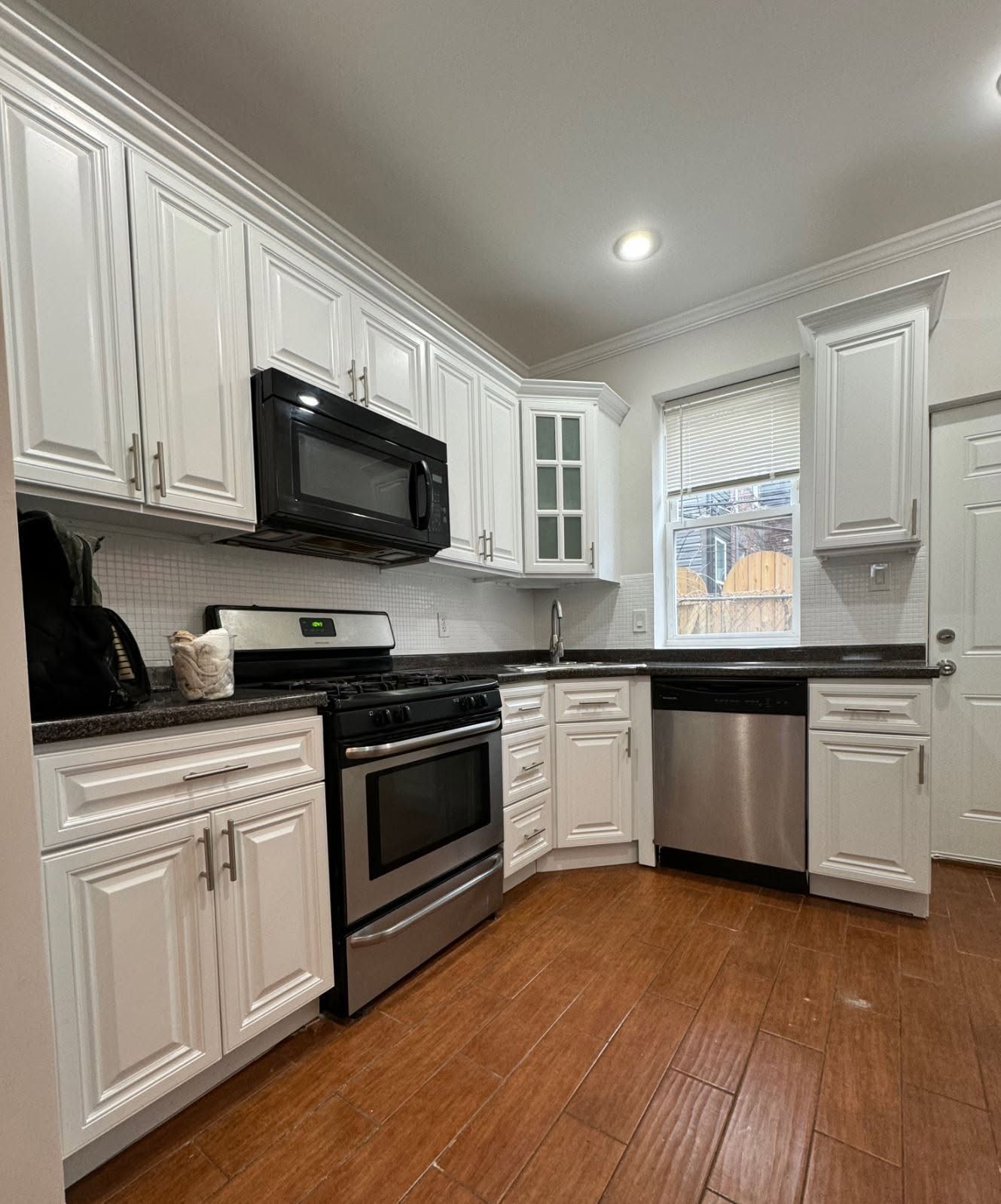 Bright white kitchen with stainless appliances, black countertops, and wood floors.