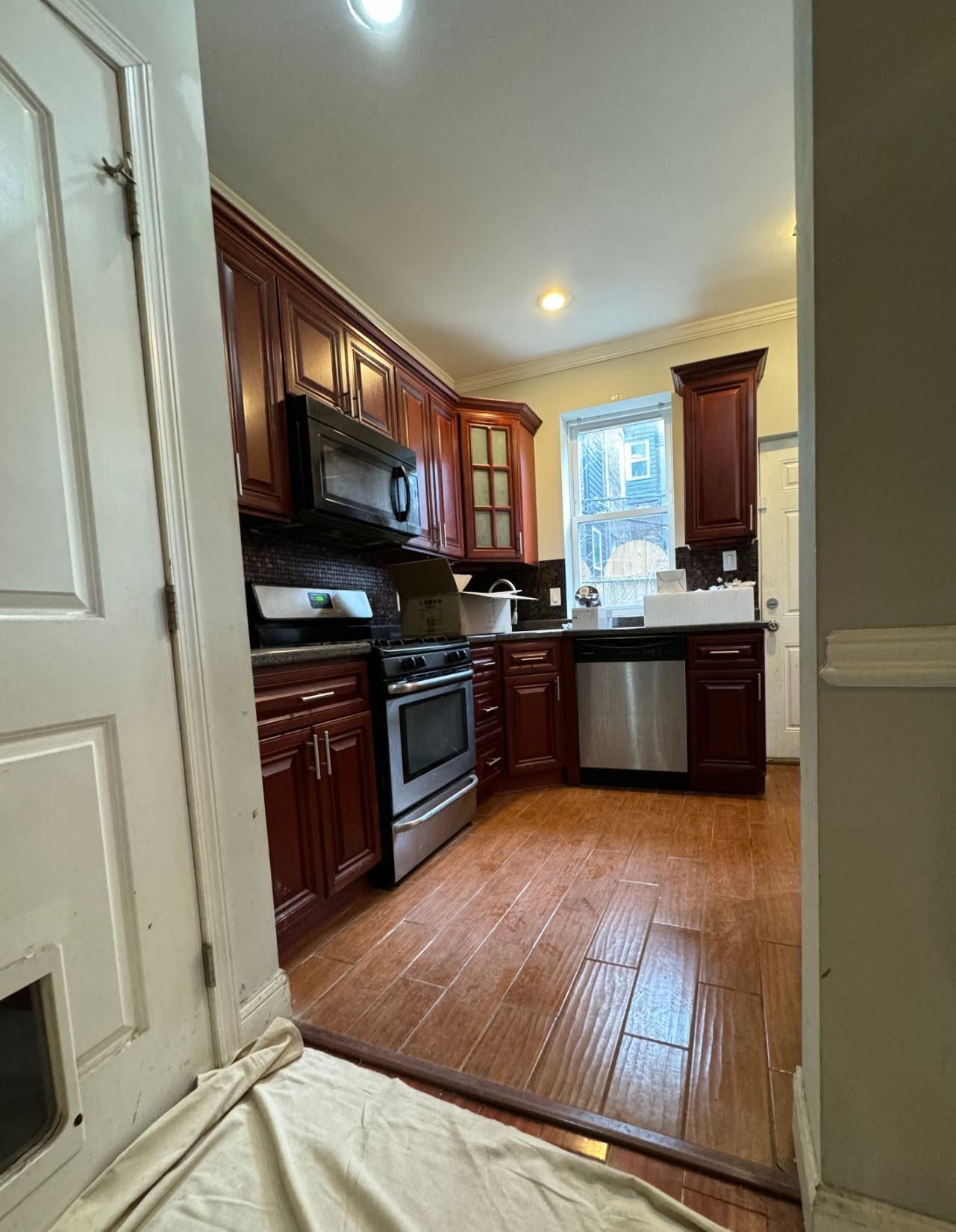 Compact kitchen with dark wood cabinets, stainless appliances, and a window above the sink on a tiled floor.
