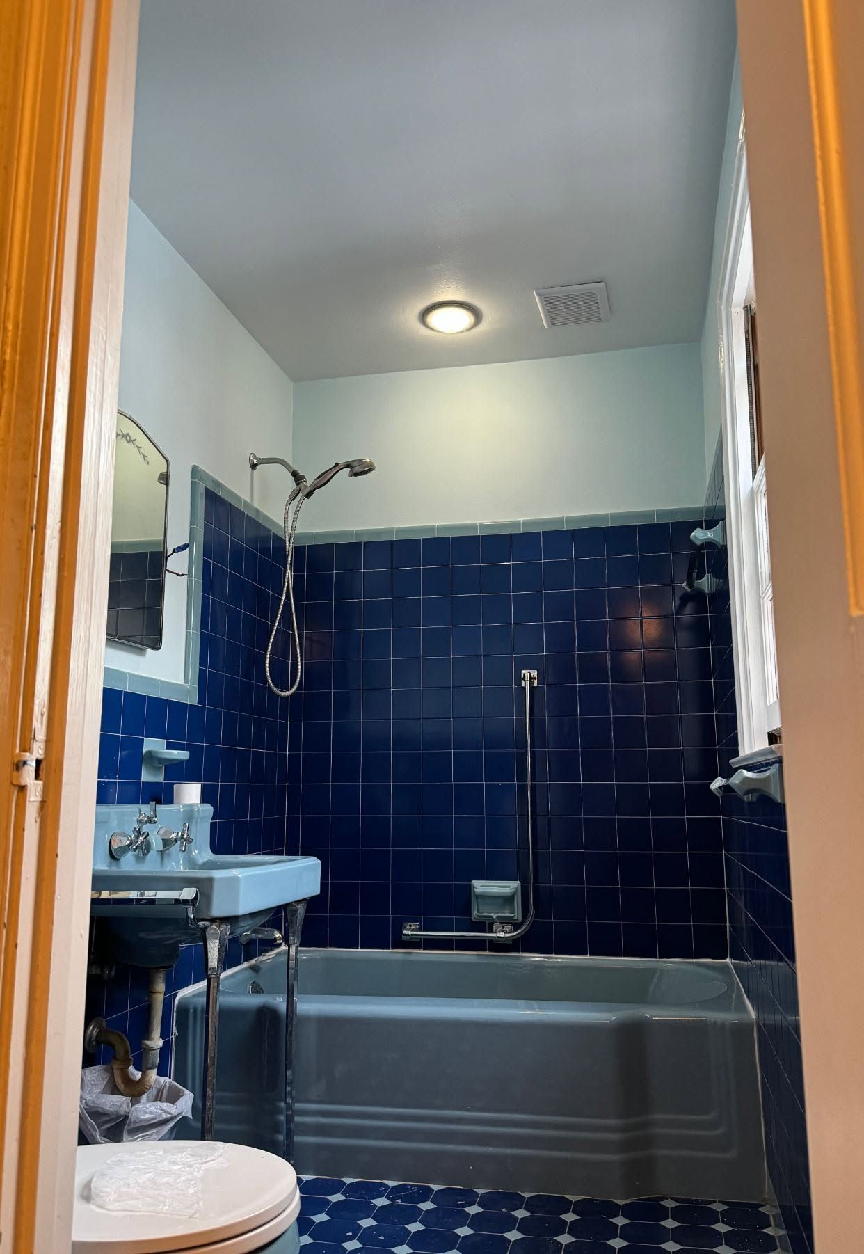 Small bathroom with a gray tub, dark blue tile walls, sink, toilet, and showerhead.