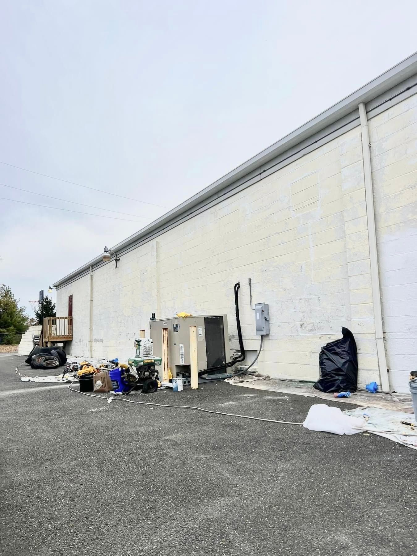 Exterior of a white warehouse wall with trash bins, scattered debris, and a forklift on a gravel lot