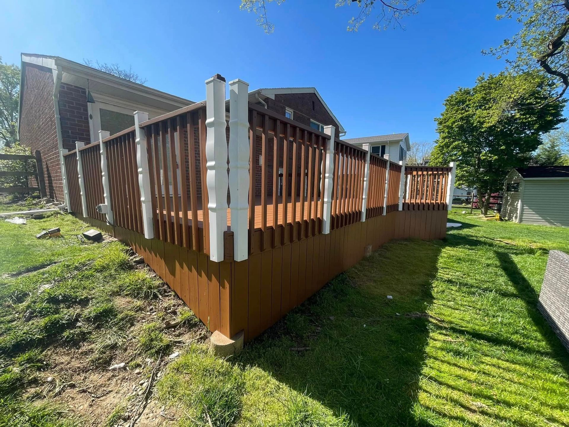Wooden deck with white railings beside a brick house on a sunny day