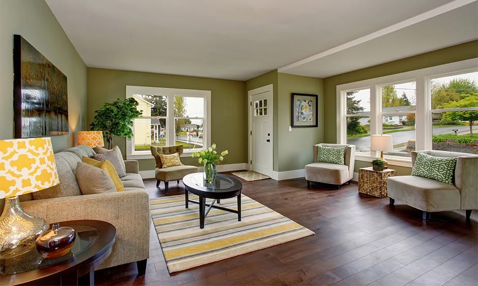 Bright living room with beige sofas, green walls, striped rug, and large windows overlooking a yard
