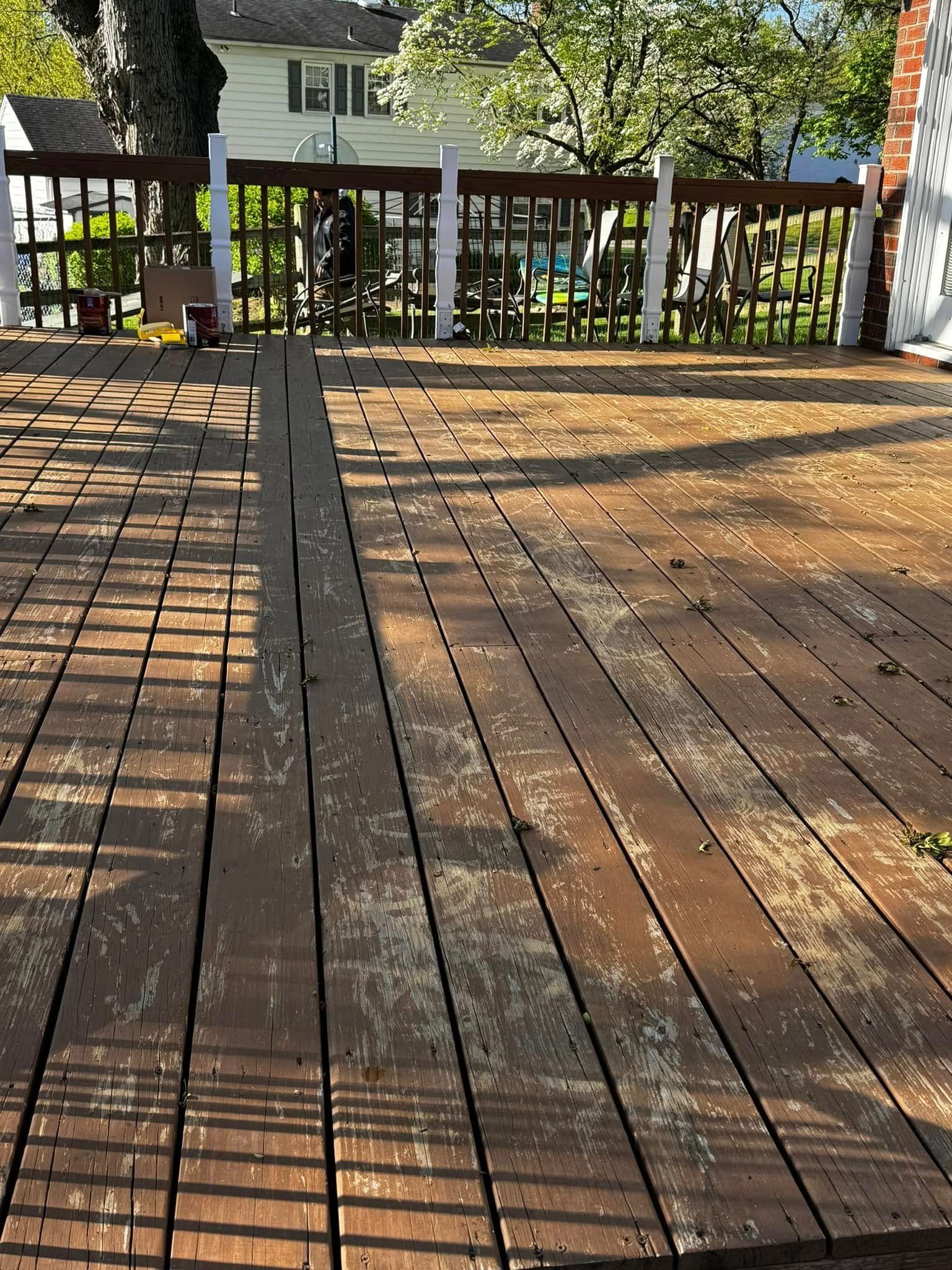 Wooden deck with a railing, dappled sunlight, and a yard visible beyond the fence.