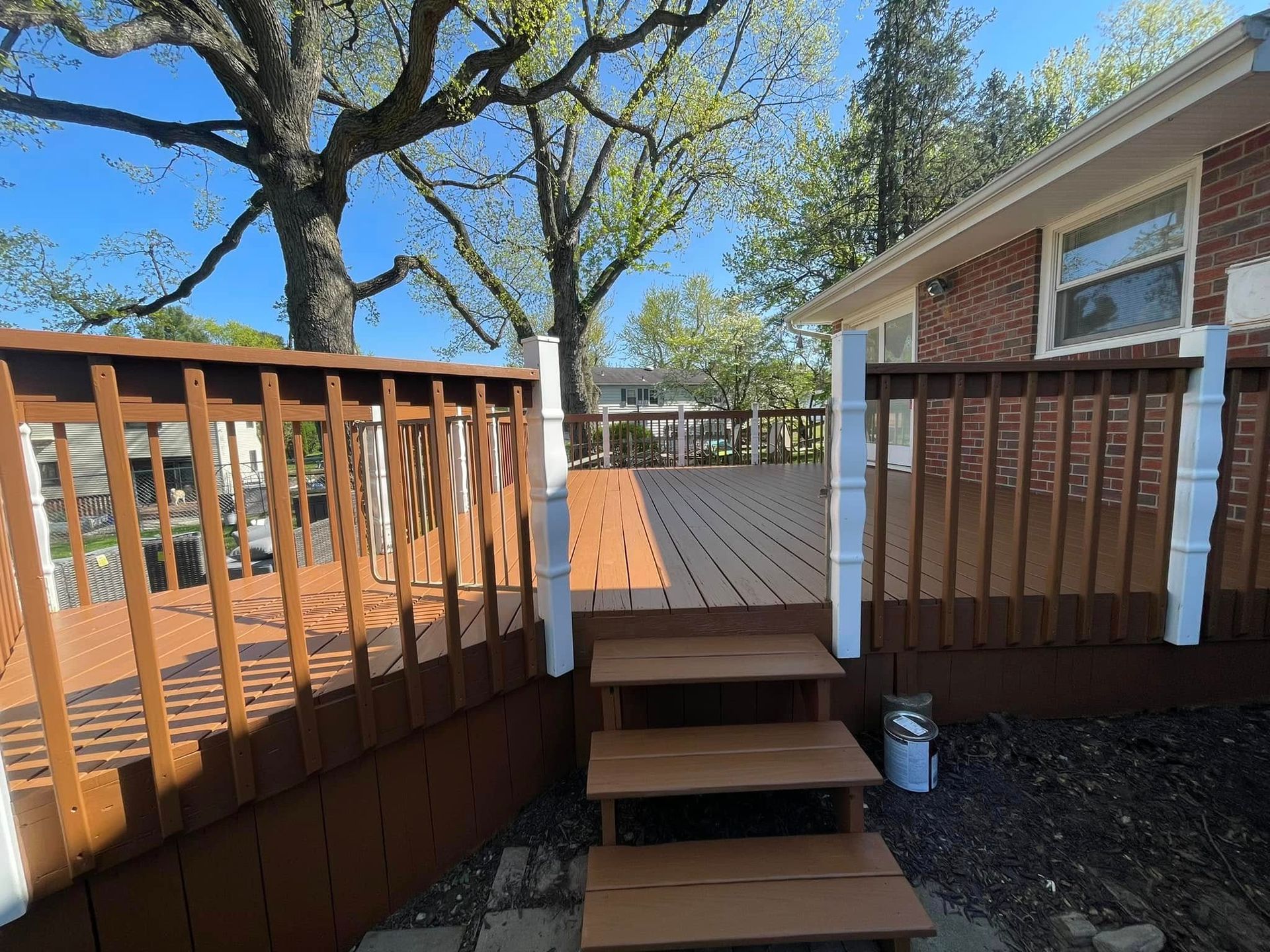 Wooden deck steps leading to a raised backyard deck beside a brick house under a blue sky