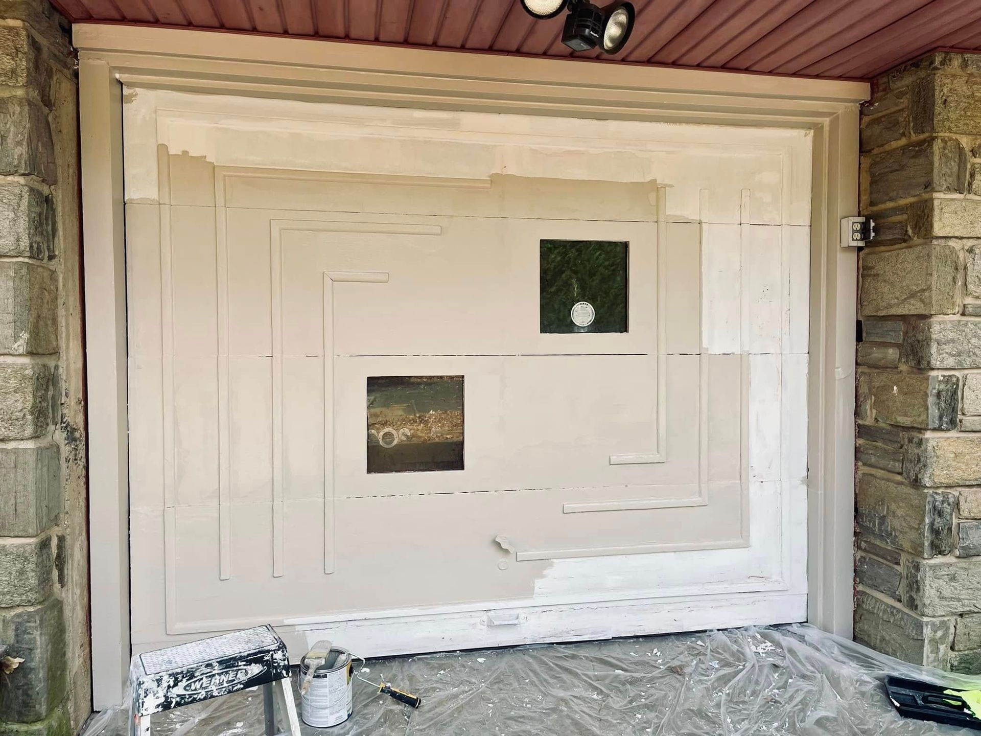 White garage door with two small windows, partially buried in snow beneath a house overhang