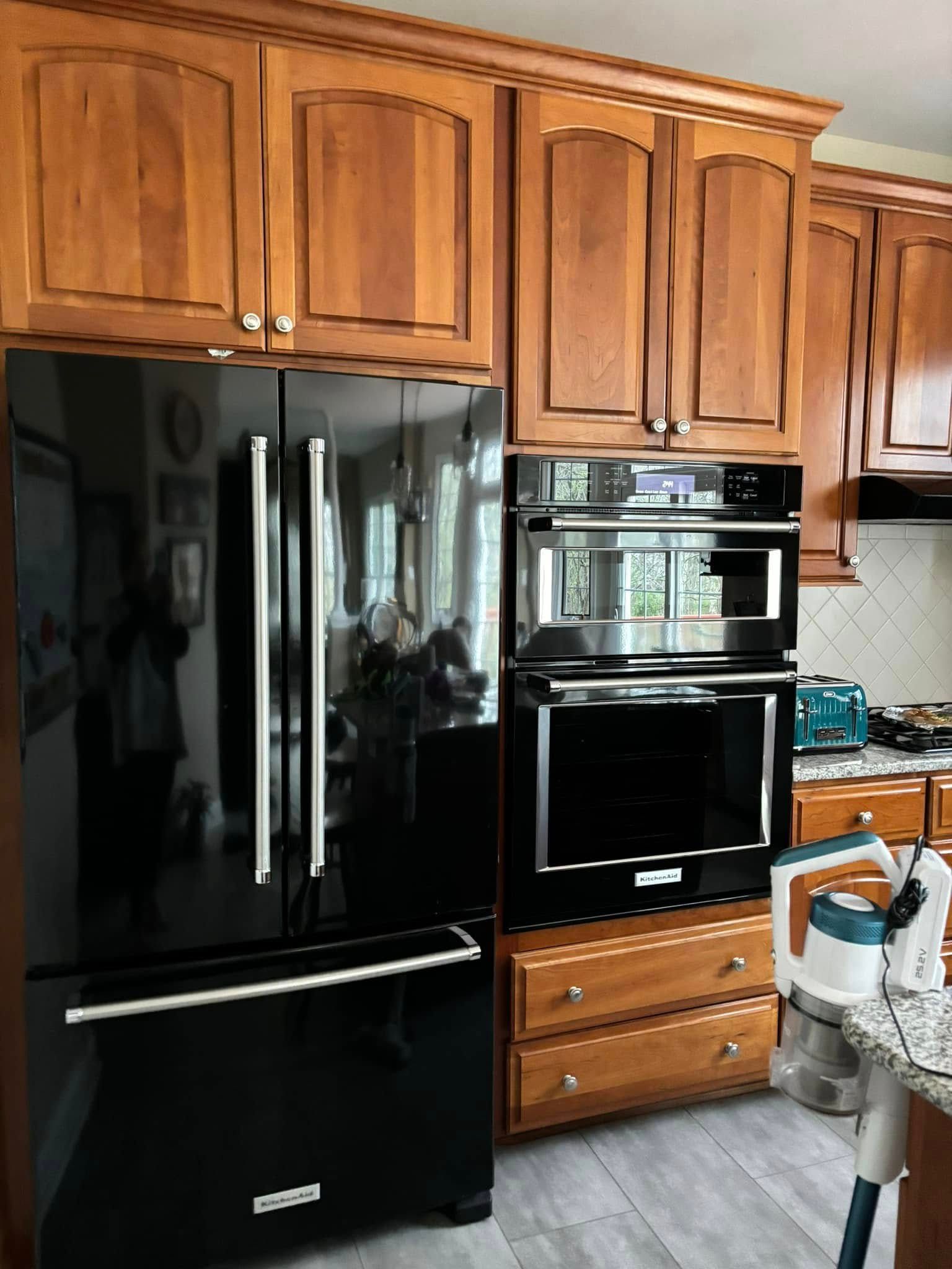 Kitchen with black refrigerator, double wall oven, and wood cabinets.