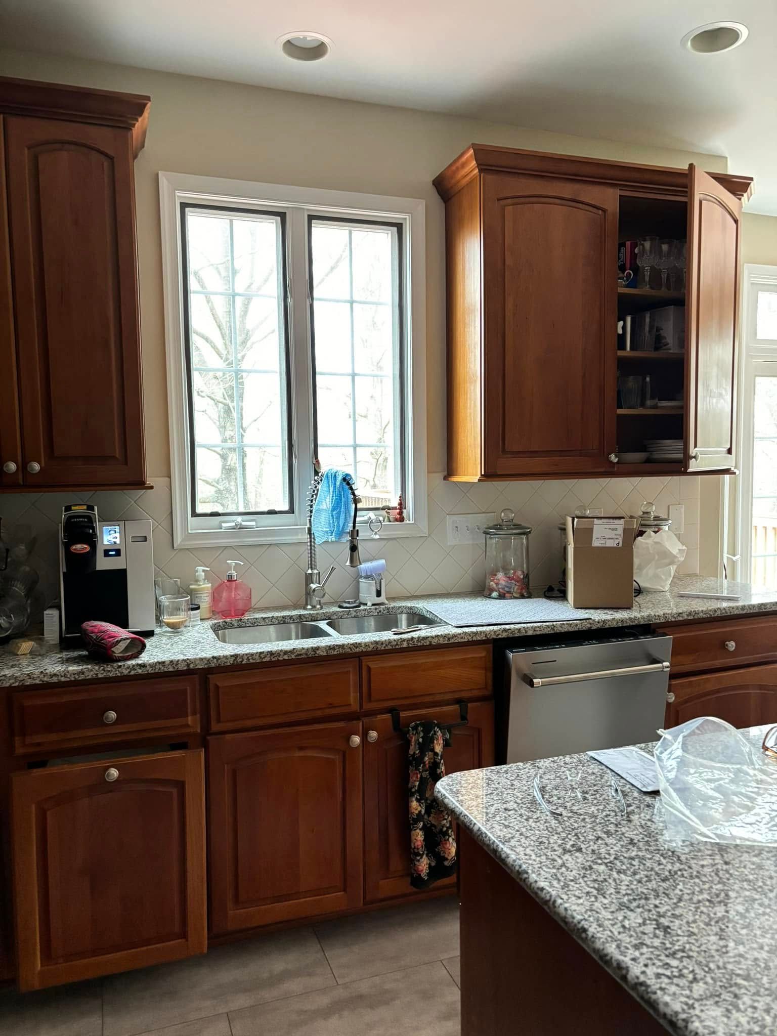 Wooden kitchen with granite countertops, sink under window, and a dishwasher beside a speckled island counter