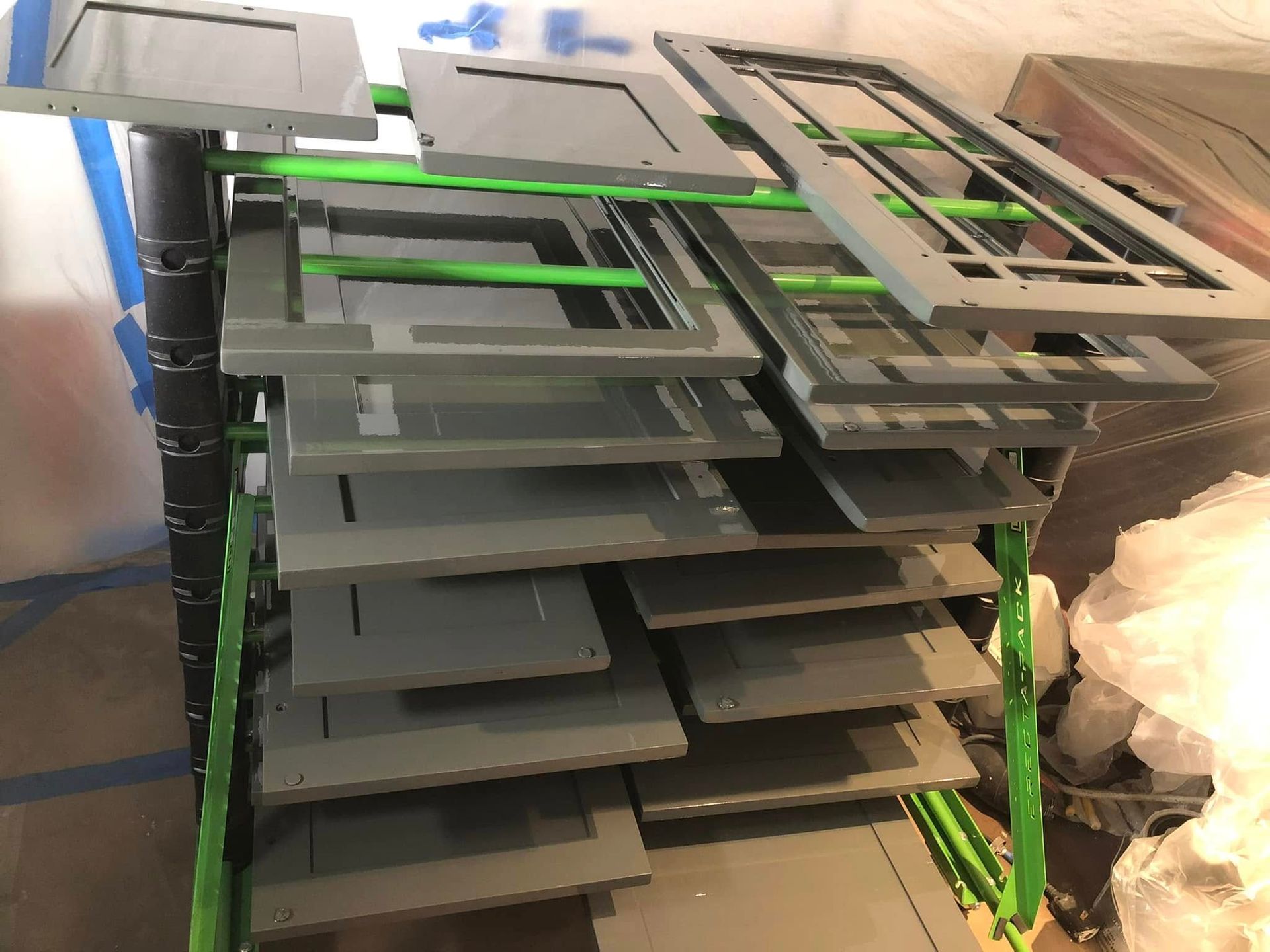 Stacked gray metal trays on green racks in an industrial storage area.